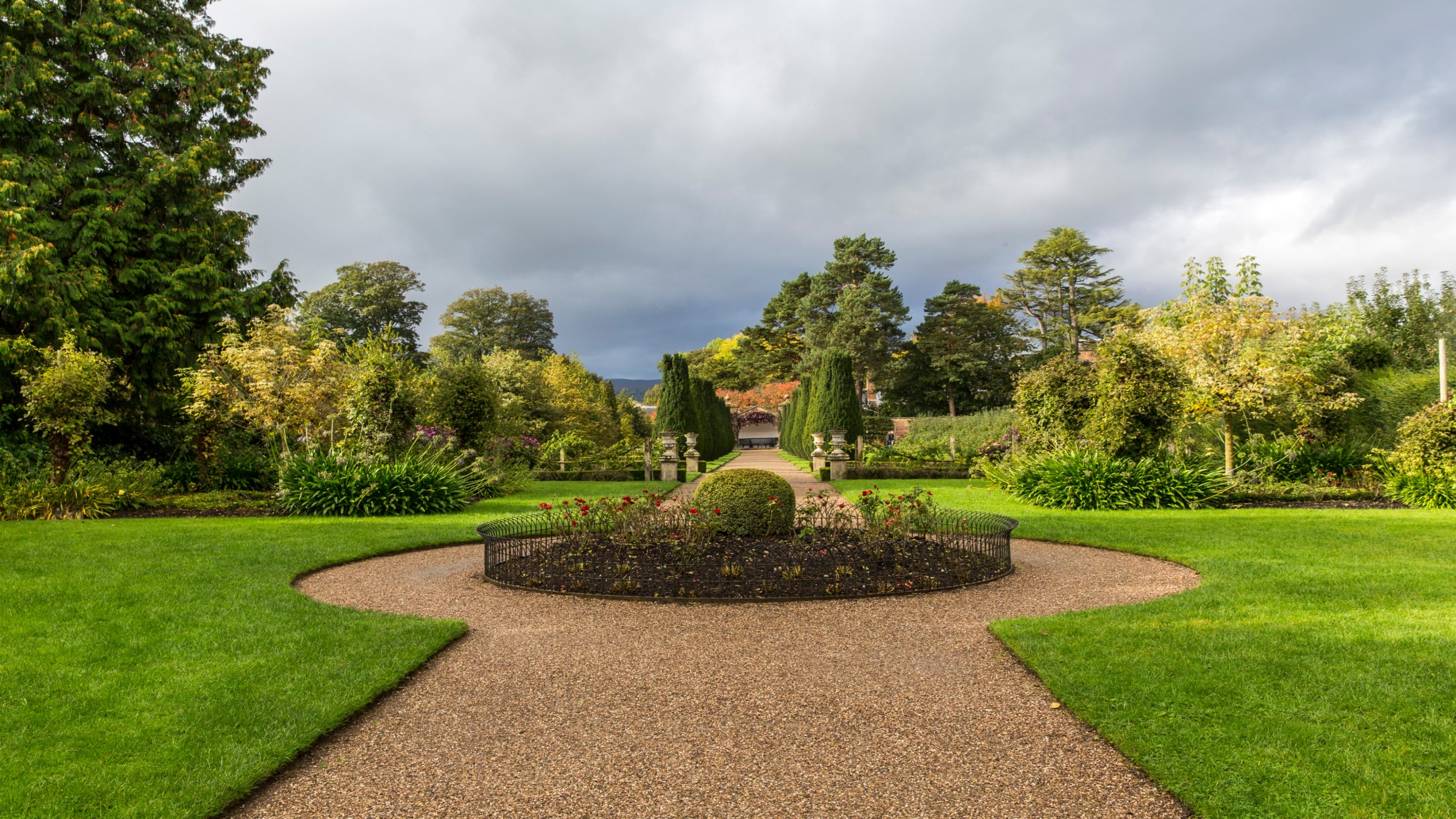 The center bedding of the Victorian garden, featuring flower beds with a variety of plants. In the distance, yew trees form a walk.