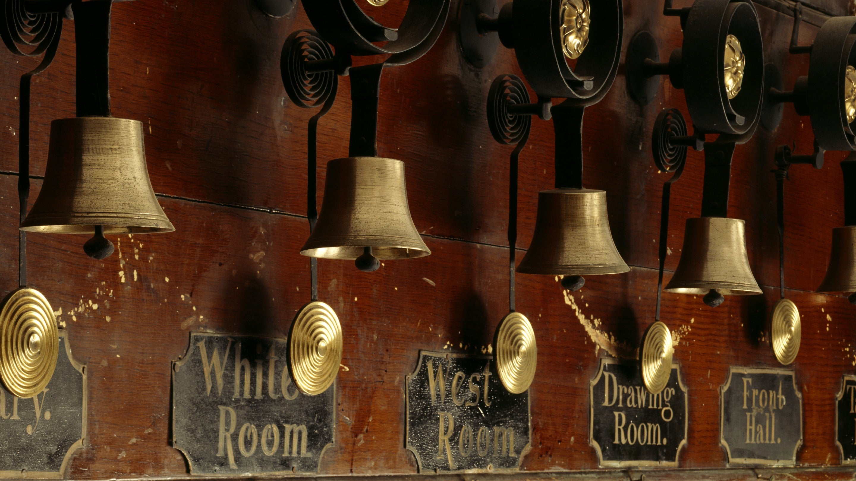 Bwrdd pren gyda chlychau efydd. Maent wedi eu labelu ‘White Room’, ‘West Room’, ‘Drawing Room’ a ‘Front Hall’.