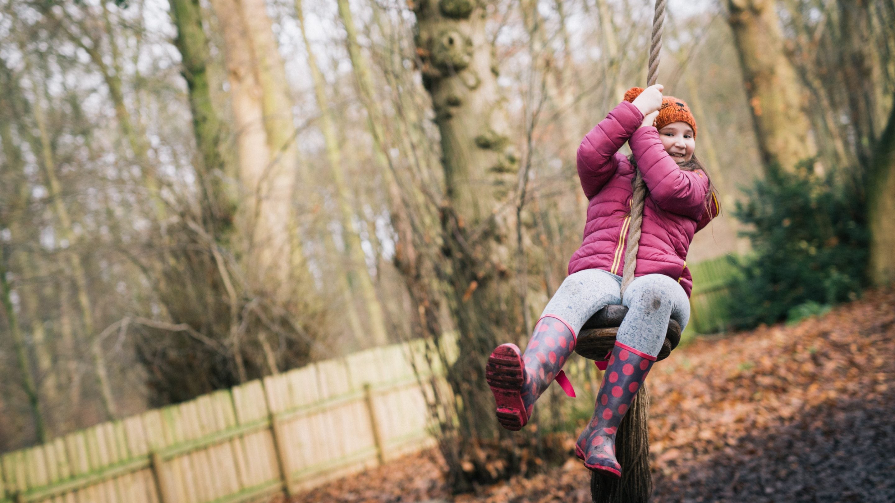 A girl wearing brightly coloured winter clothes on a rope swing