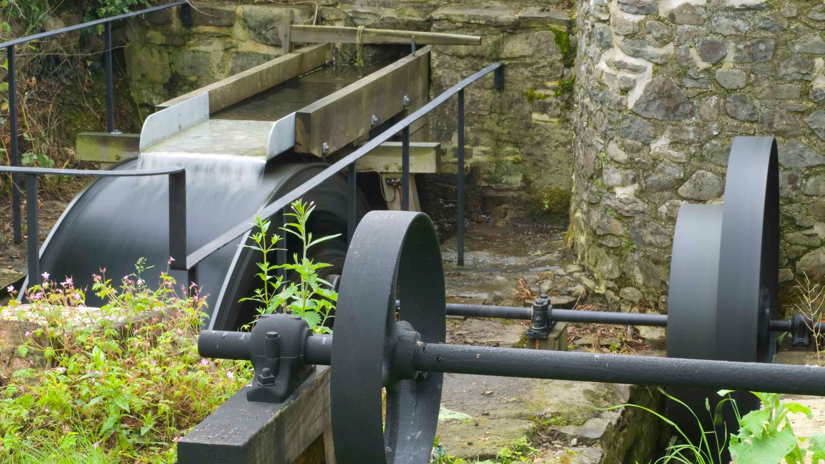 Gweithrediad mecanyddol olwyn ddŵr yn dangos dŵr yn llifo ar hyd gyli a thrwy wal ac olwyn ddŵr yn troi’n gyflym.