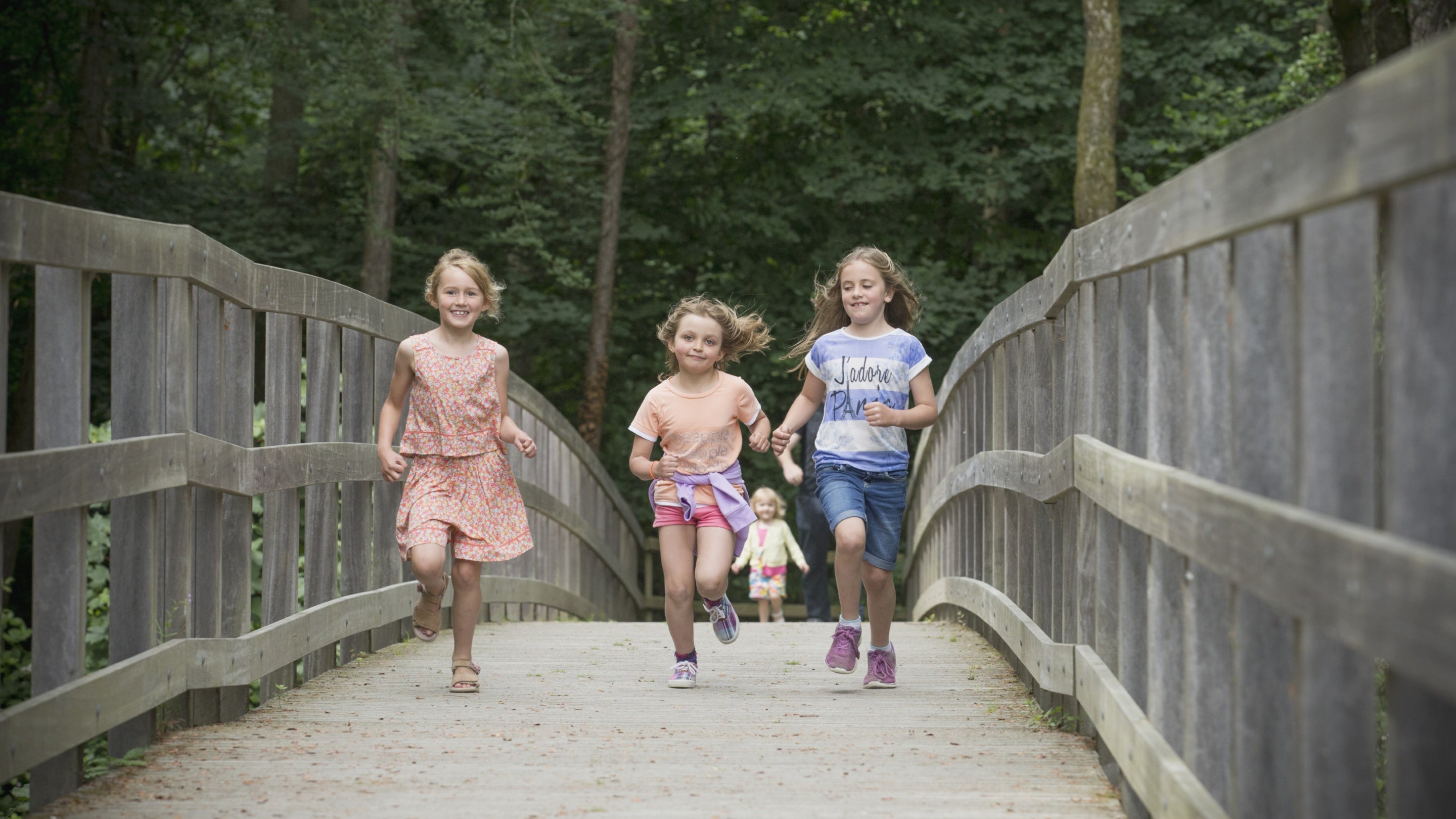 Three girls running across the bridge at Llanerchaeron in Ceredigion, Wales
