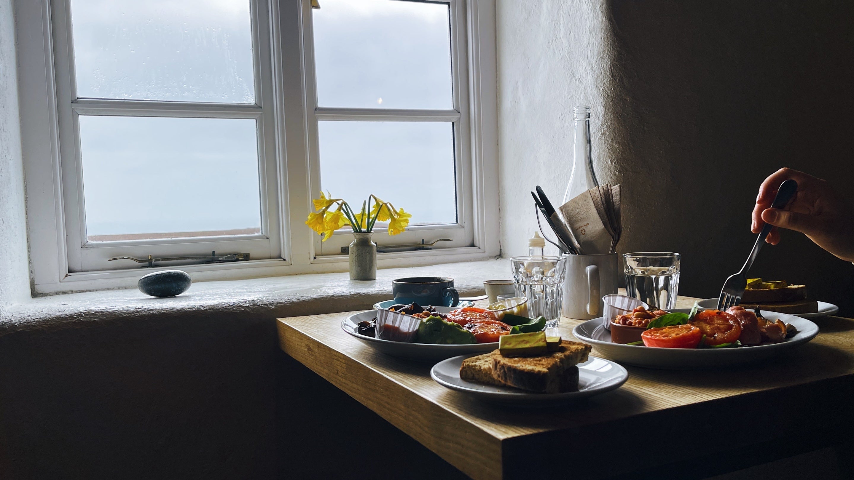 Traditional and vegan breakfast served on a table for two with a view of the sea at Runwayskiln café Marloes.