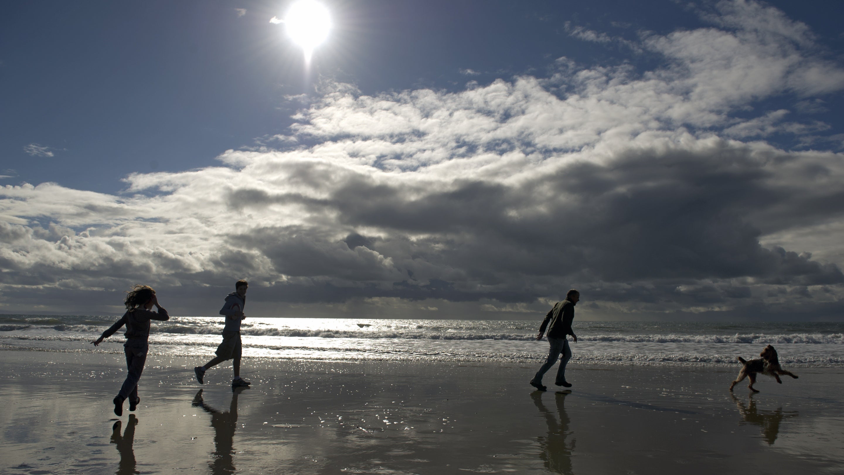 Three people playing on the beach with a dog at Pennard, Gower, Wales.