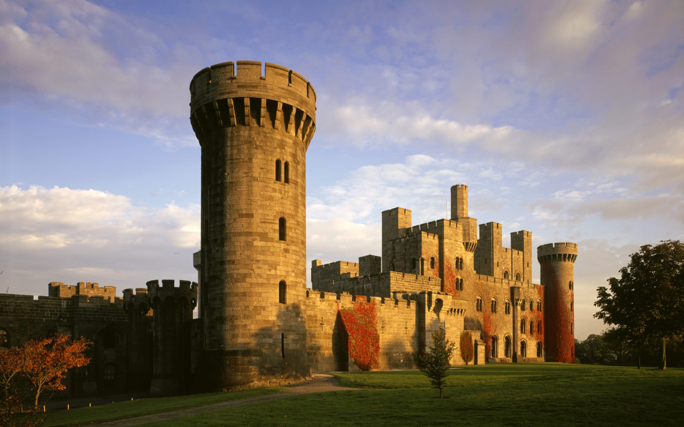 The West front of Penrhyn Castle, lit by a low sun. Trees are visible in the foreground.