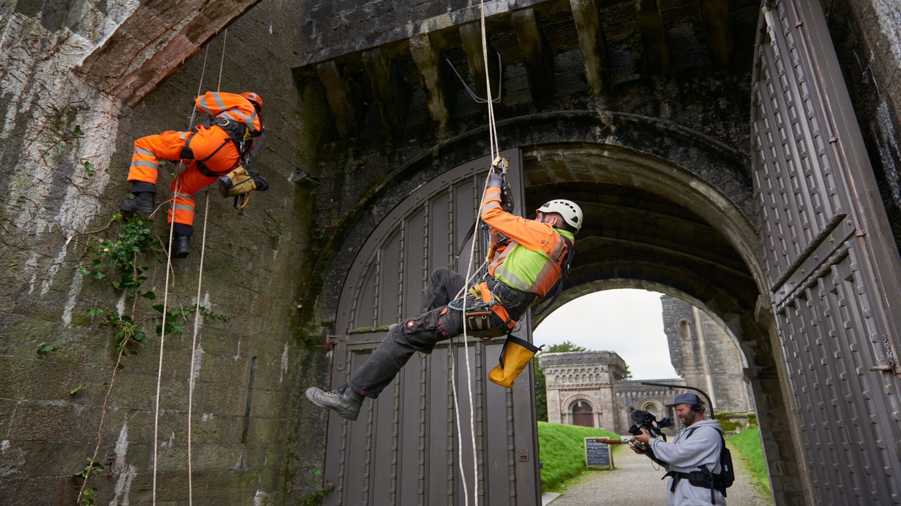 Two people on ropes on an archway door of the castle and being filmed by a third person