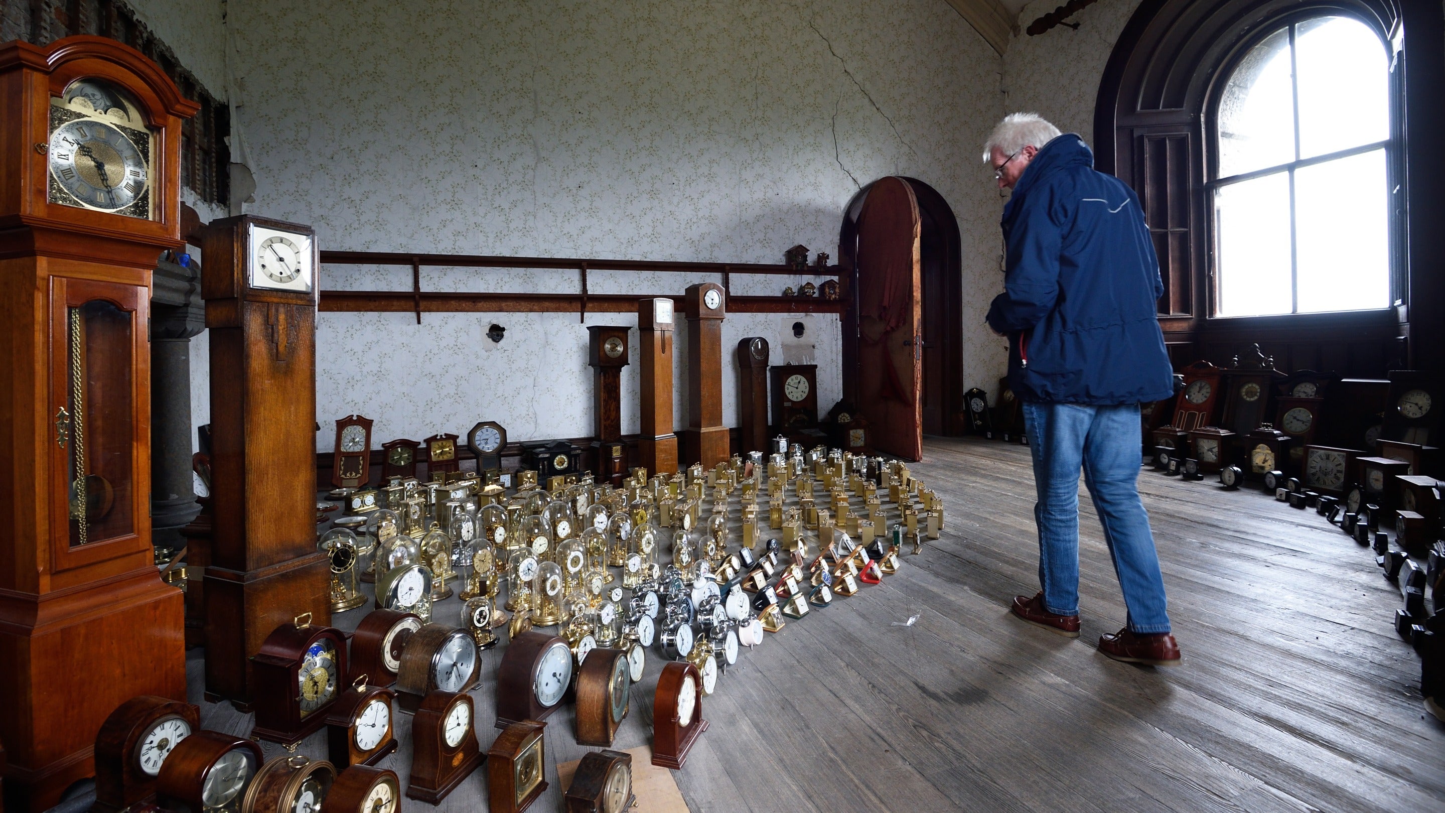 Visitor walking past hundred of clocks in the Harrison’s Garden installation by Luke Jerram, in the tower at Penrhyn Castle, Wales