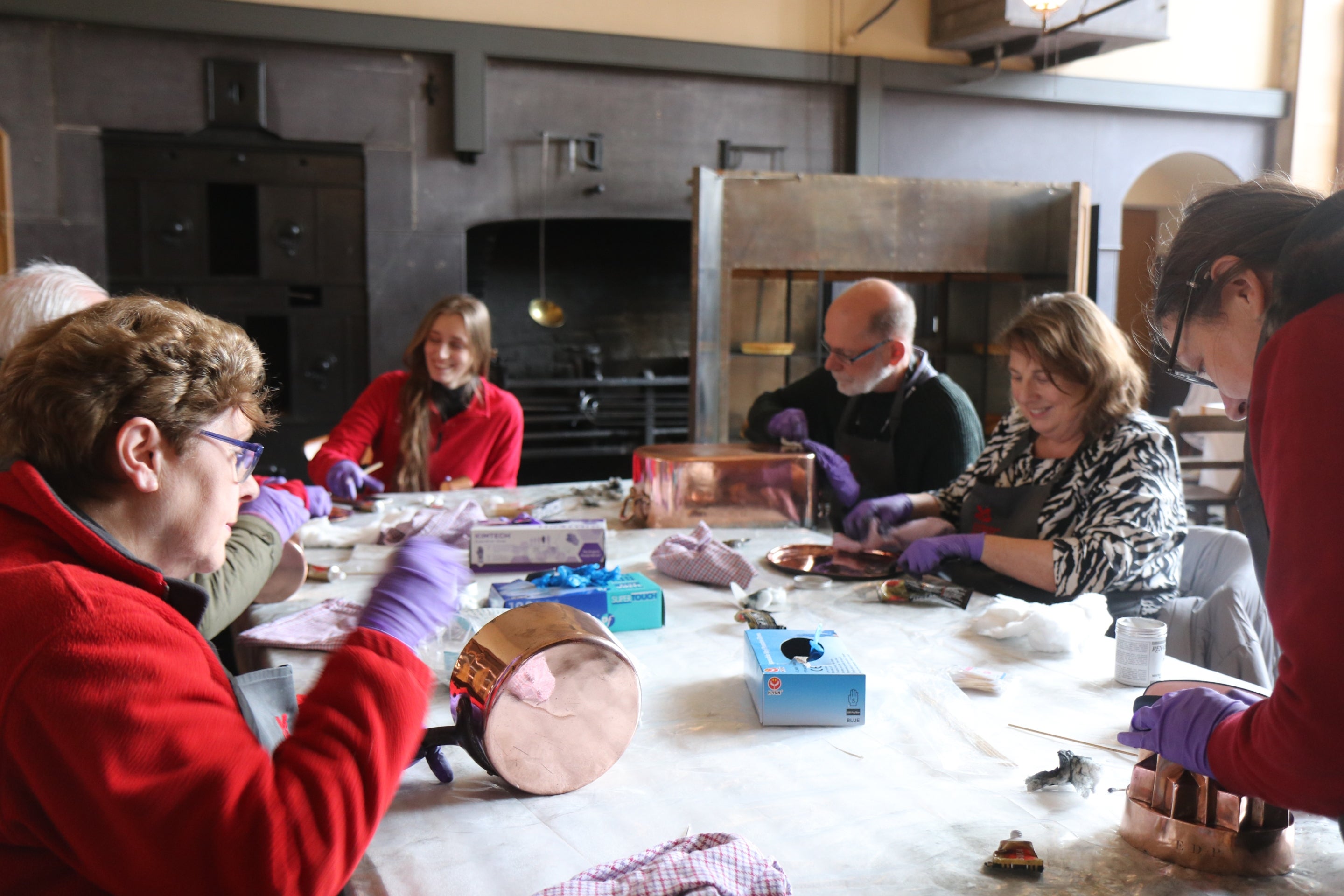 A group of staff and volunteers sit cleaning the copper items in the castle collections in the Victorian Kitchens