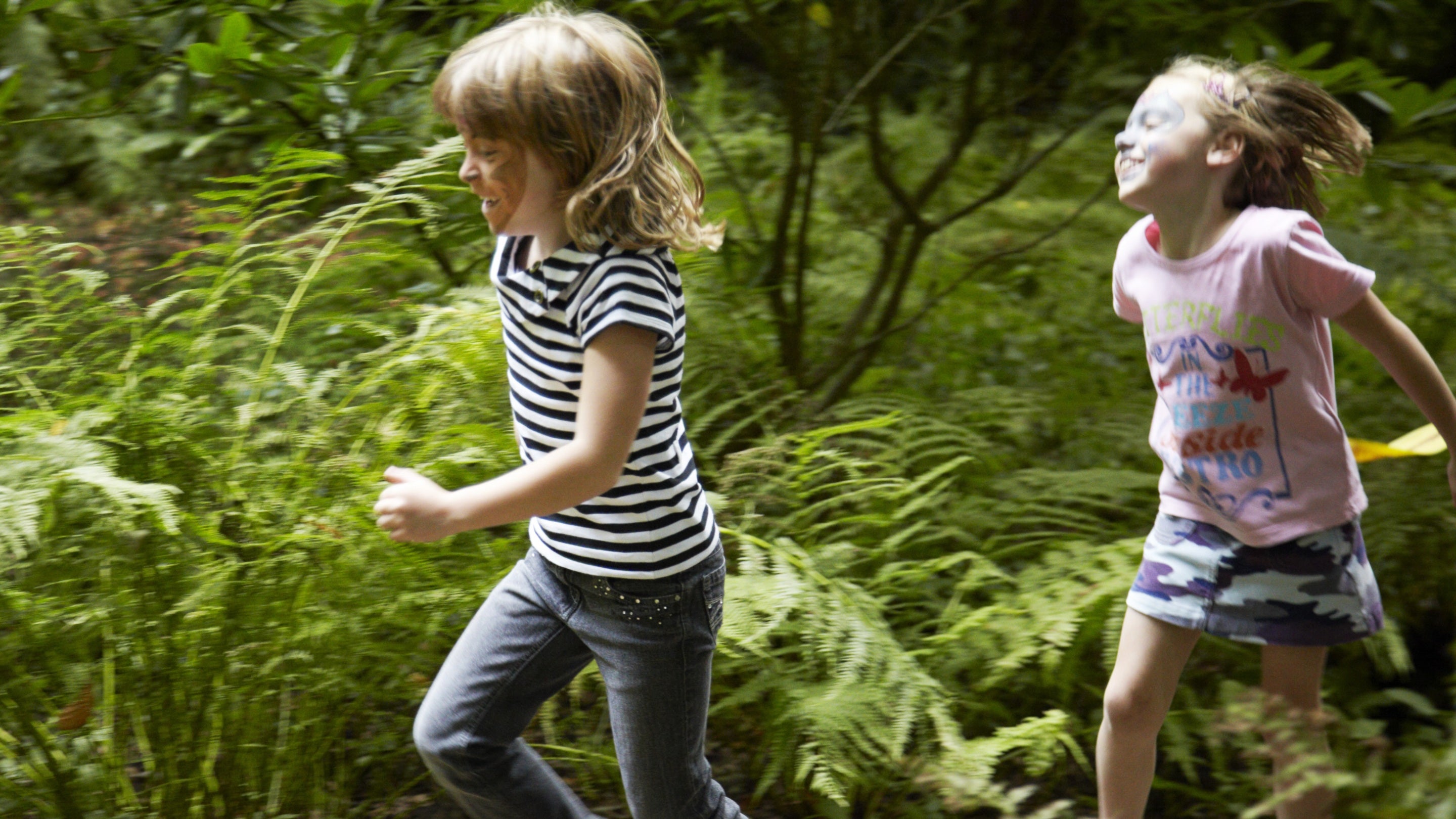 Plant yn rhedeg ar hyd llwybr trwy redyn yn yr ardd yng Nghastell Penrhyn, Gwynedd, Cymru