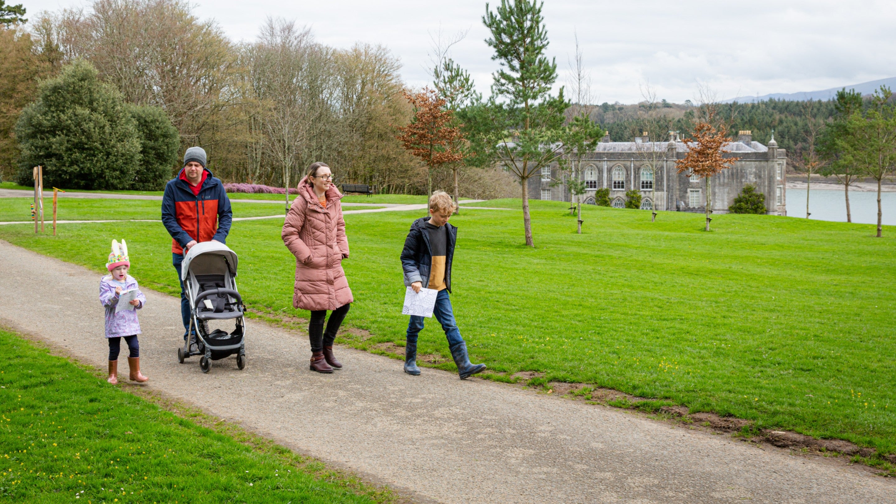 Teulu gyda phram ar antur yn yr ardd ym Mhlas Newydd, Cymru