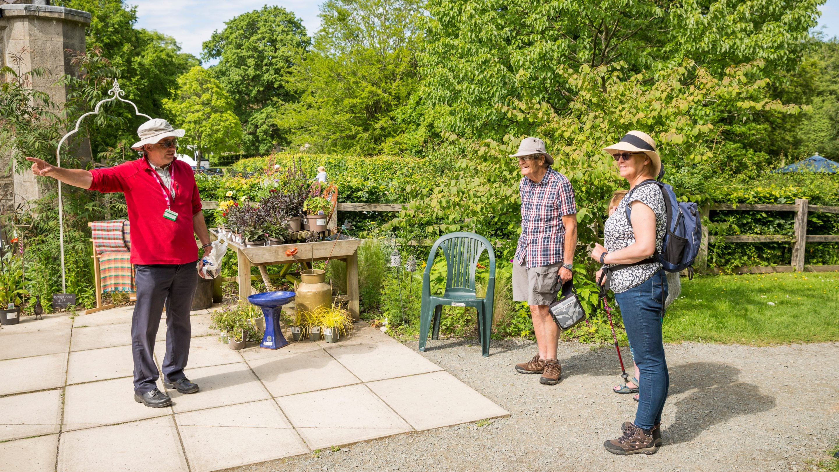 Gwirfoddolwr yn siarad ag ymwelwyr ar ddiwrnod heulog yn yr ardd ym Mhlas Newydd, Ynys Môn, Gogledd Cymru