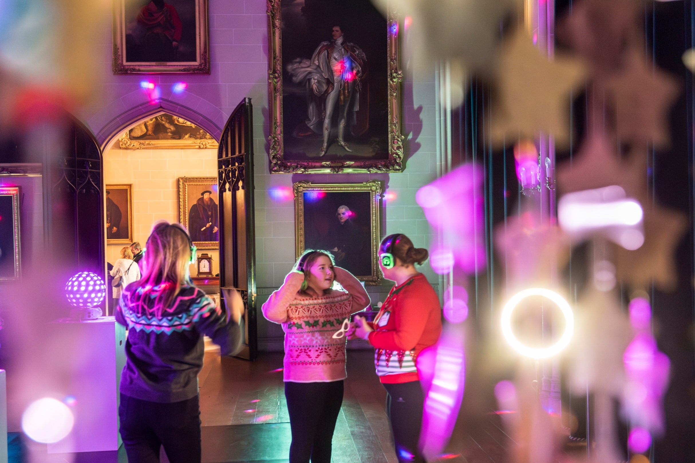 People with headphones dancing in a silent disco at Plas Newydd with disco lights reflecting on walls