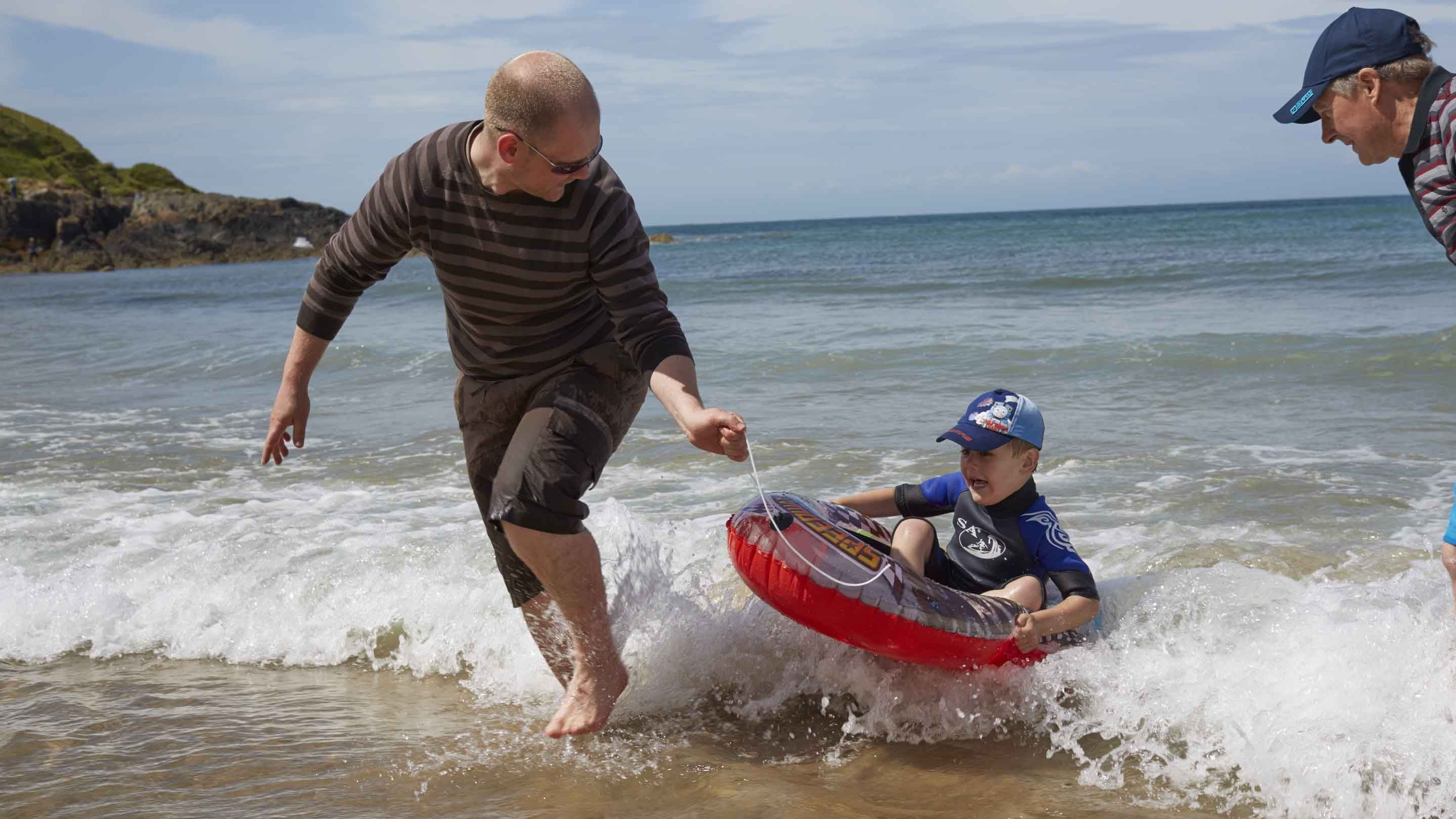 Man pulling a child on an inflatable in the sea at Whistling Sands, Porthor, Gwynedd