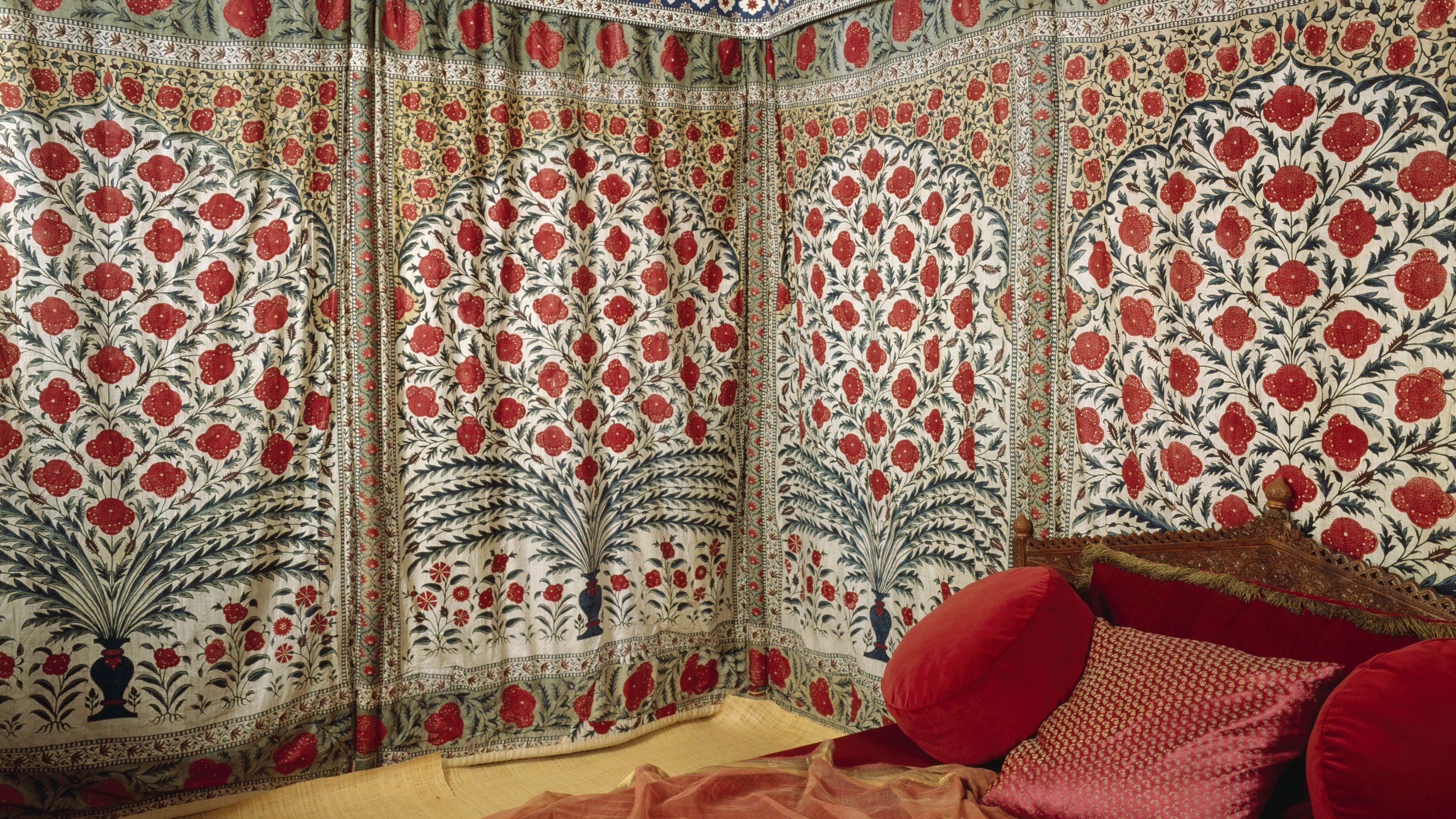 An image of fabric wall panels from Tipu Sultan's tent made from fine cotton chintz with a white ground, patterned with acanthus enclosing a central vase with symmetrical flower arrangement, predominantly in reds and greens