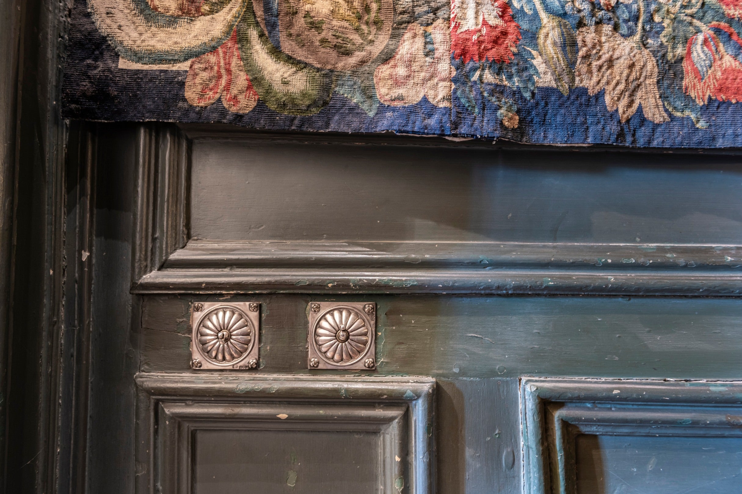 A silver light switch on a blue wall below a tapestry