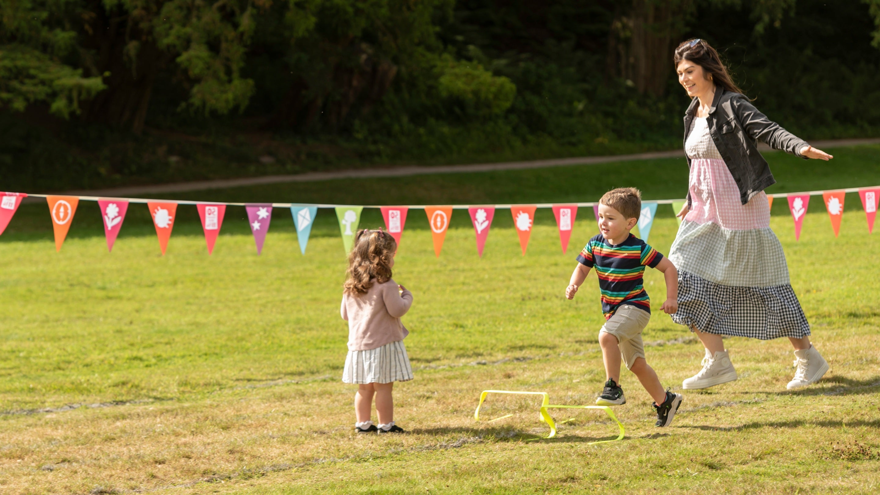 An adult running on the lawn with two small children playing on the grass