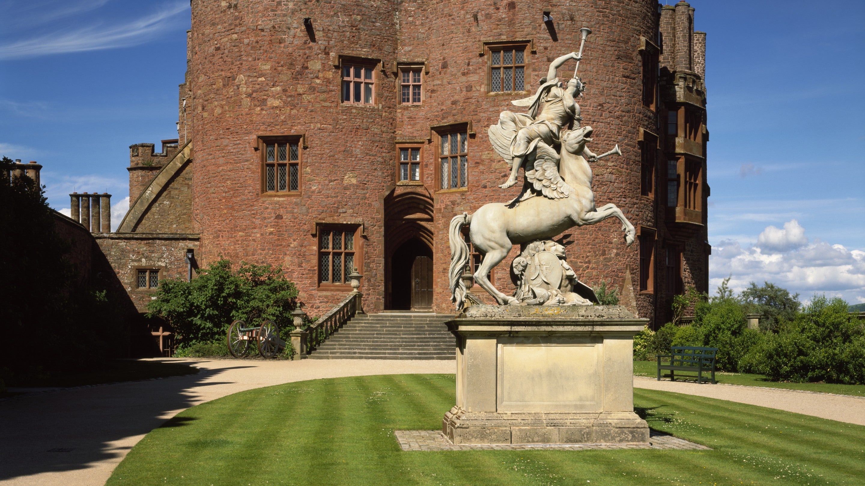 An image of a large stone statue of Fame created around 1705 by Andries Carpentiere, set on the lawn outside the west front of Powis Castle in Wales which is just in the background