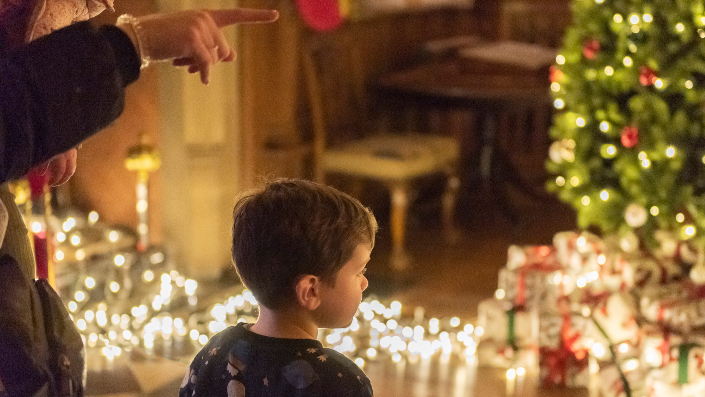 Little boy looking at Christmas tree, gifts and lights in the Dining Room at Powis Castle in Powys, Wales