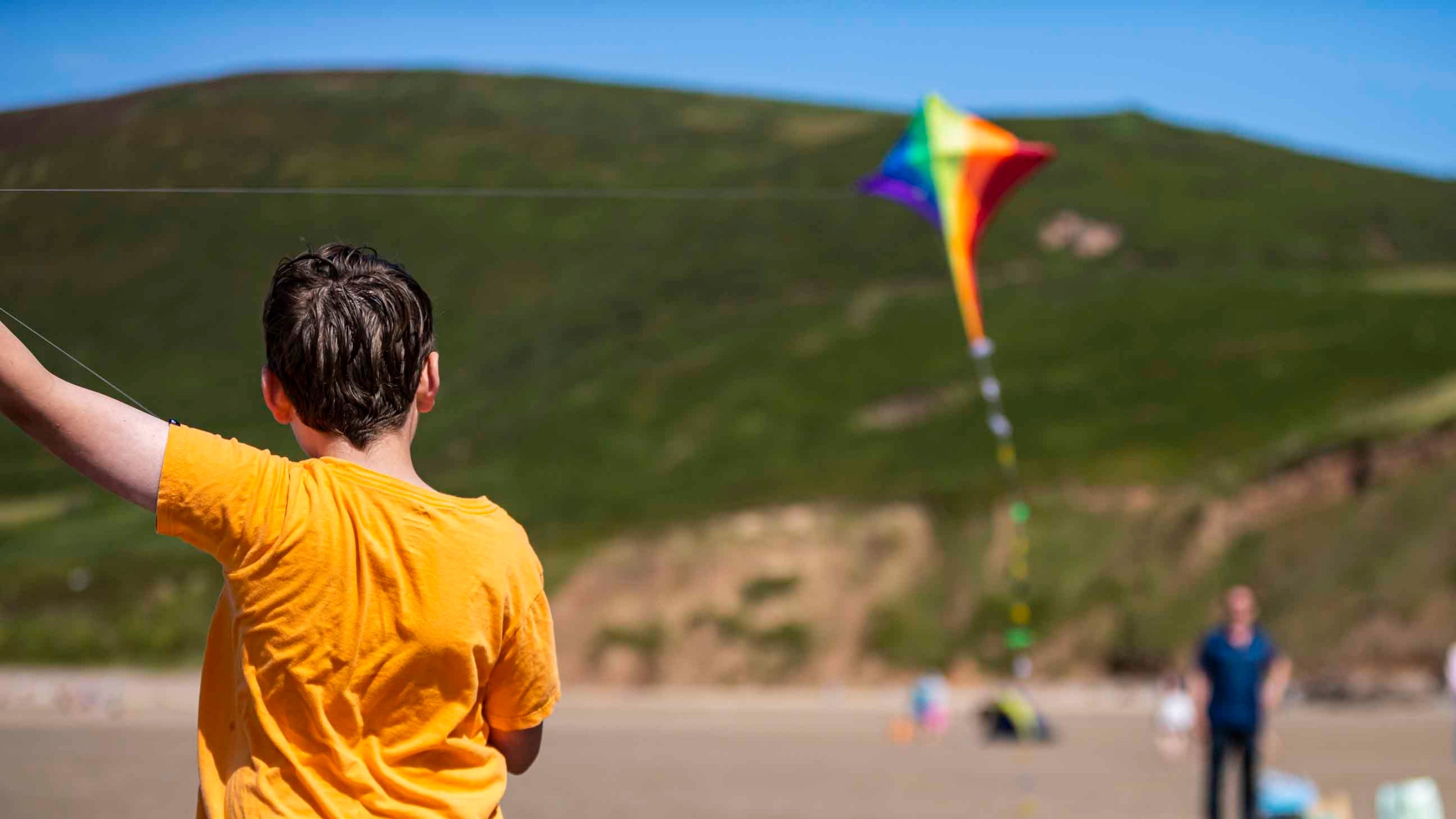 A young visitor in an orange t-shirt flying a kite on the beach at Rhosili and South Gower Coast