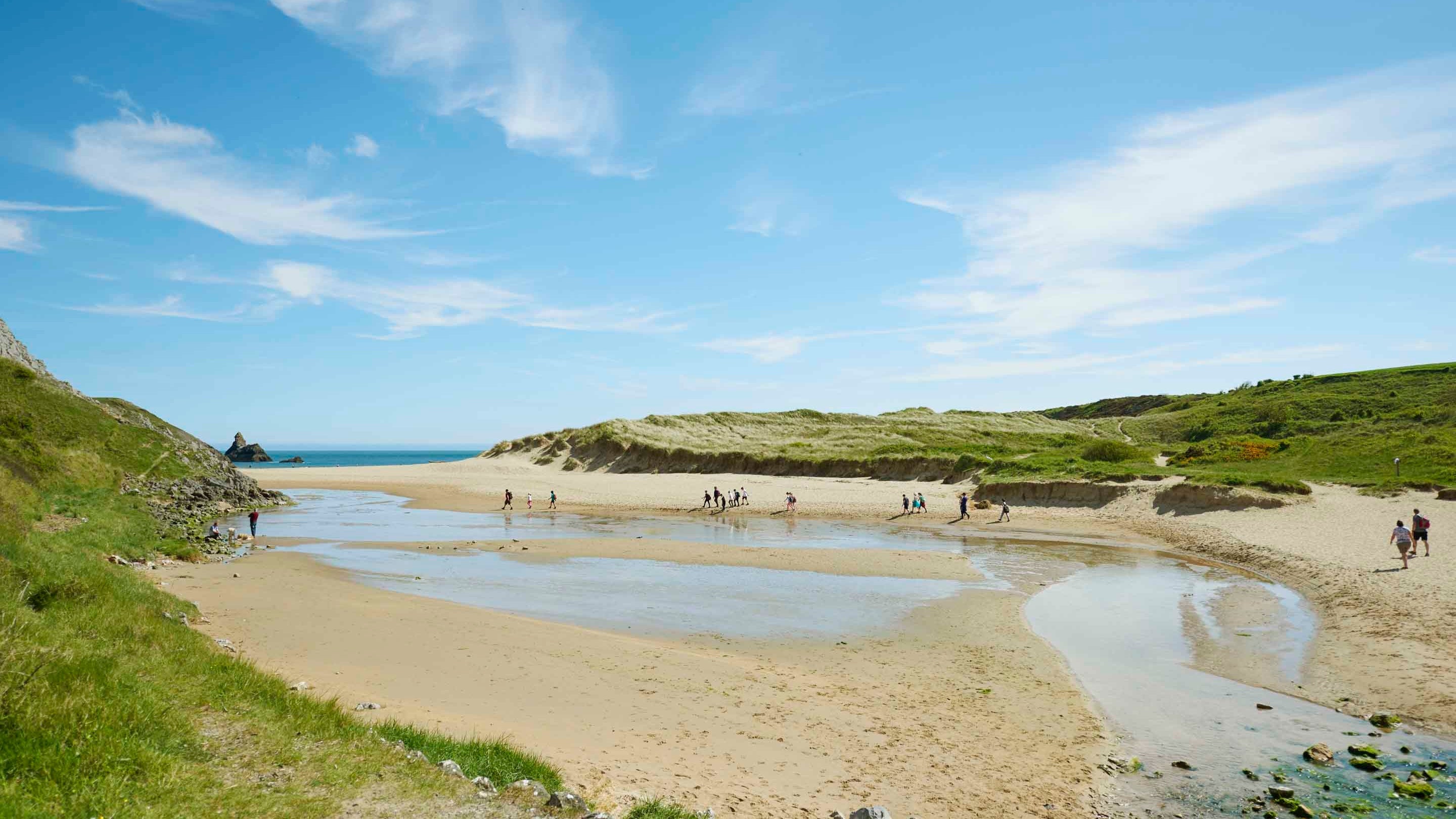 Visitors in the distance on the Broad Haven South beach at Stackpole on a sunny day with blue skies.