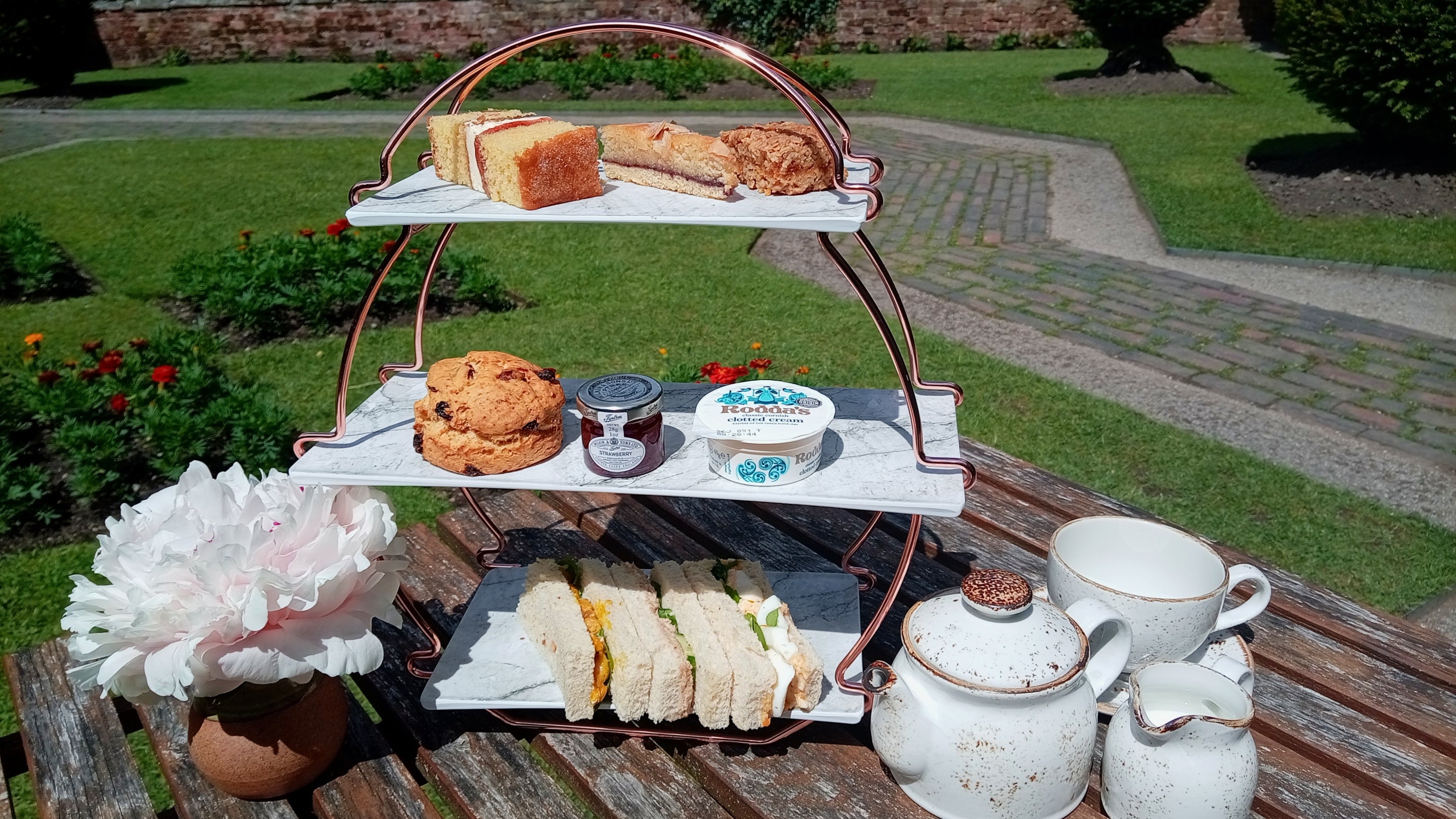 A three-tier cake stand loaded with goodies set on a table in the courtyard garden at Baddesley Clinton, Warwickshire.