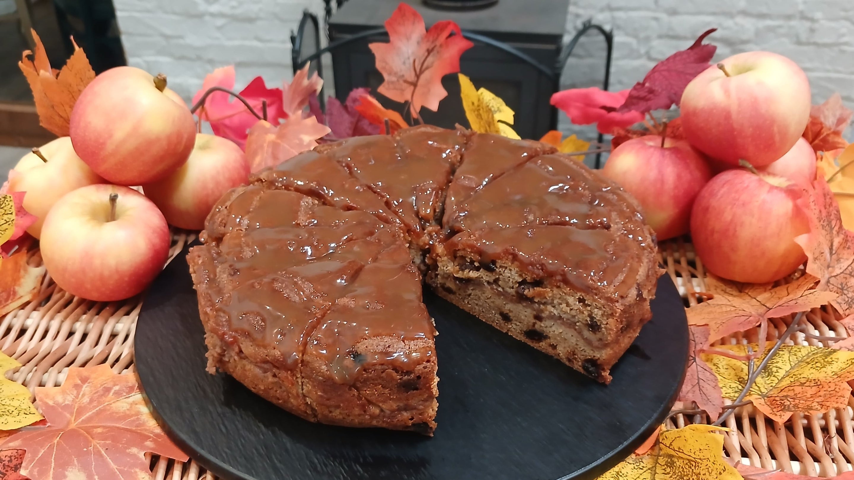 A spiced toffee apple cake on a black plate with piles of apples behind. Available at the Barn Restaurant, Baddesley Clinton, Warwickshire.