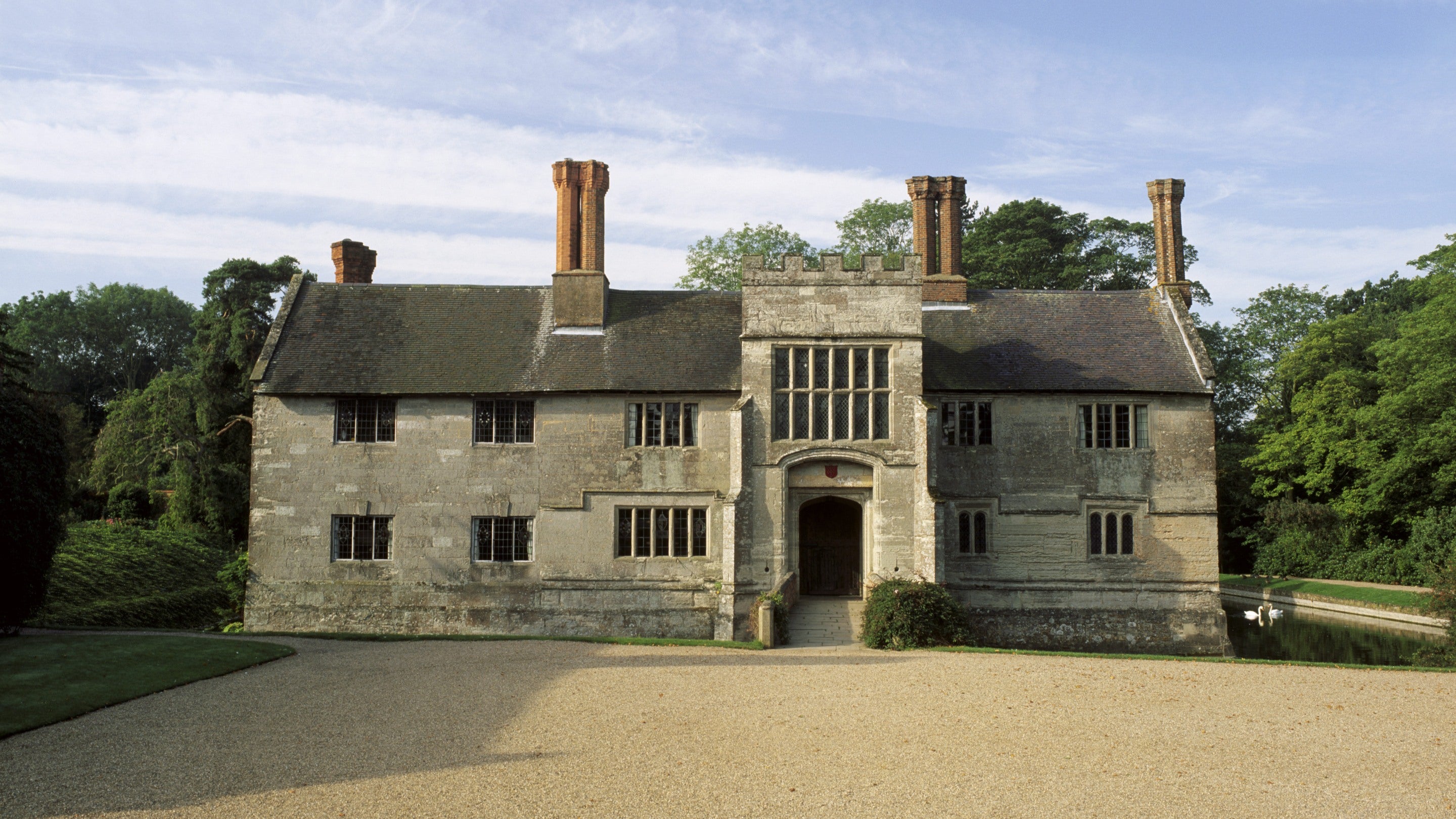 The exterior, entrance range of Baddesley Clinton in Warwickshire. A stone built house, with stone mullion windows, surrounded by a moat.