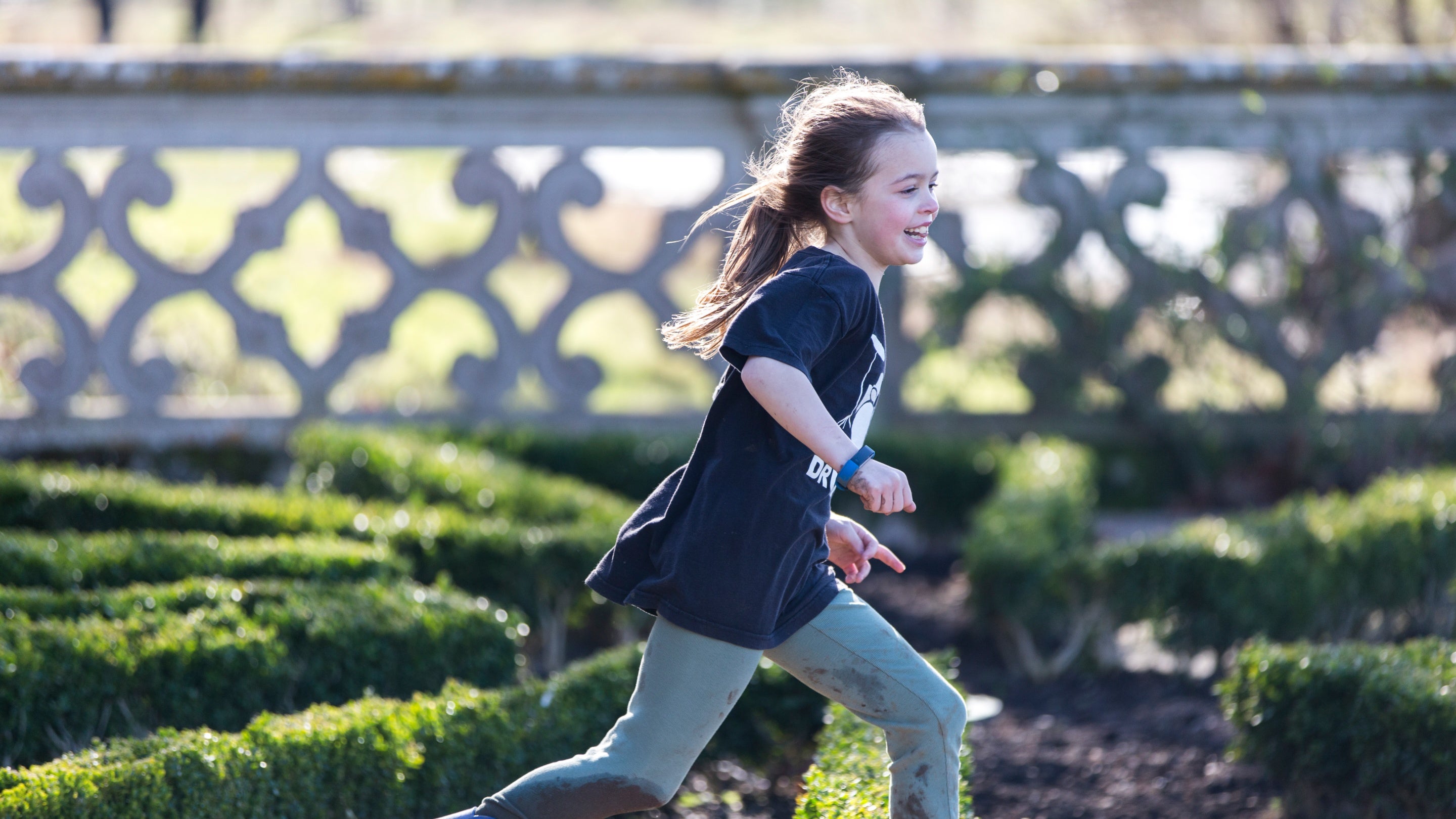 A young girl runs through the maze of low box hedging in the garden with a big smile on her face and rosy cheeks.