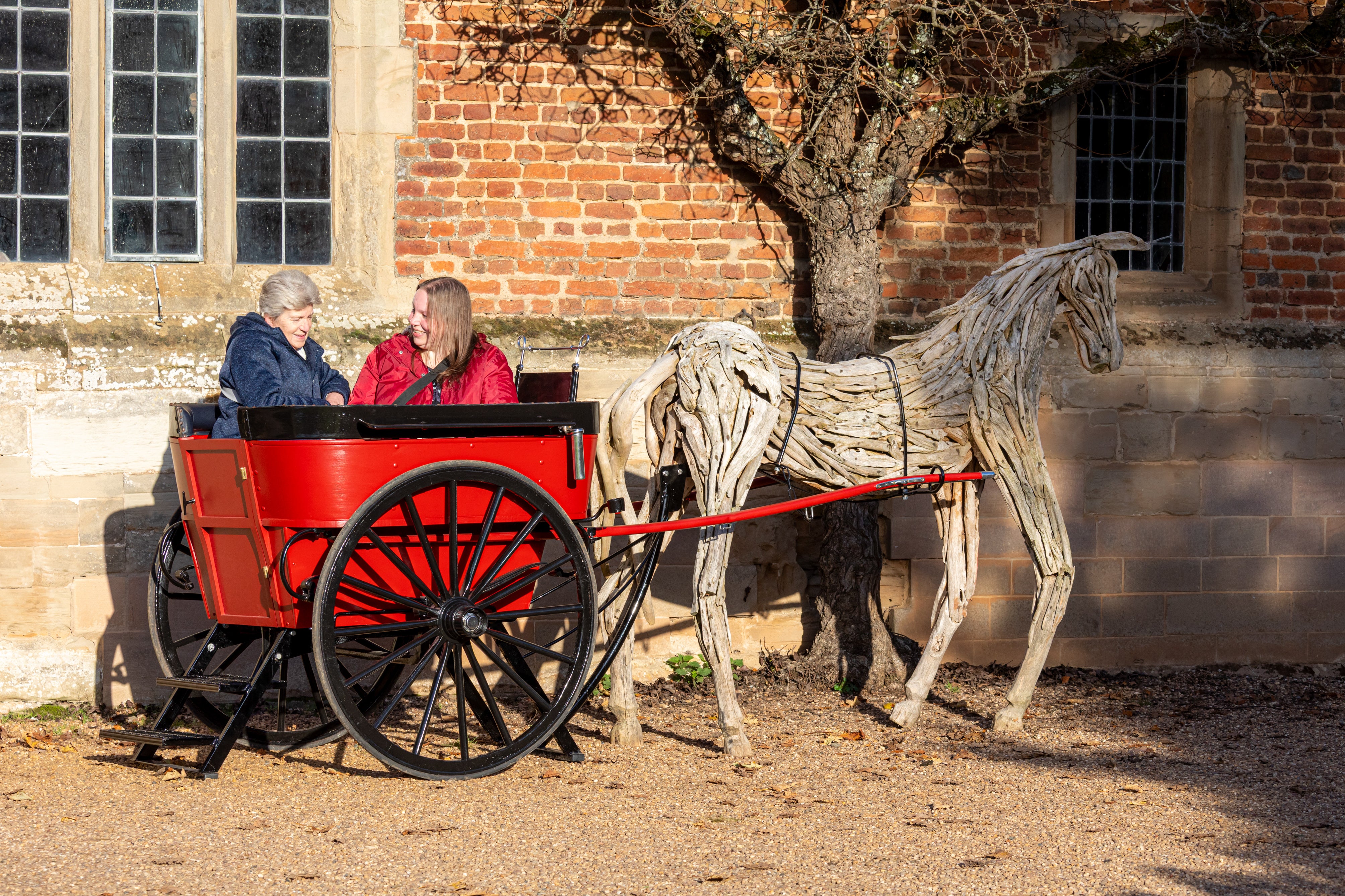 A small, red-painted governess cart and wooden horse hitched to the cart stand in the Service Courtyard