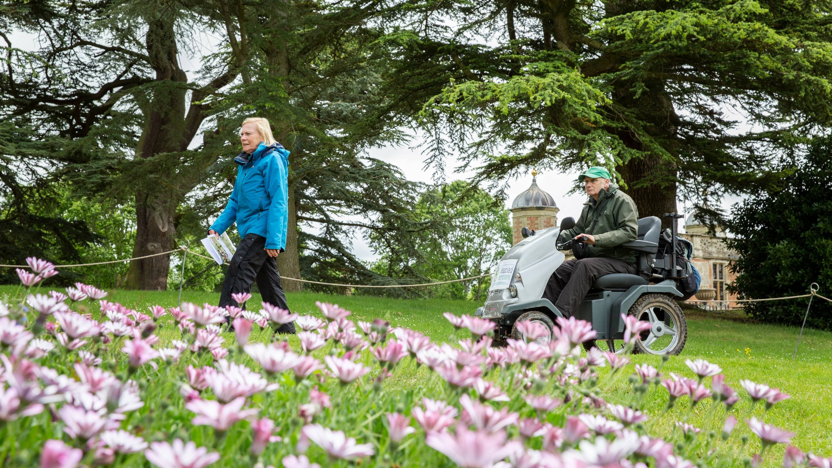 Two visitors exploring the parkland in spring at Charlecote Park, Warwickshire. One visitor is using an all terrain mobility scooter