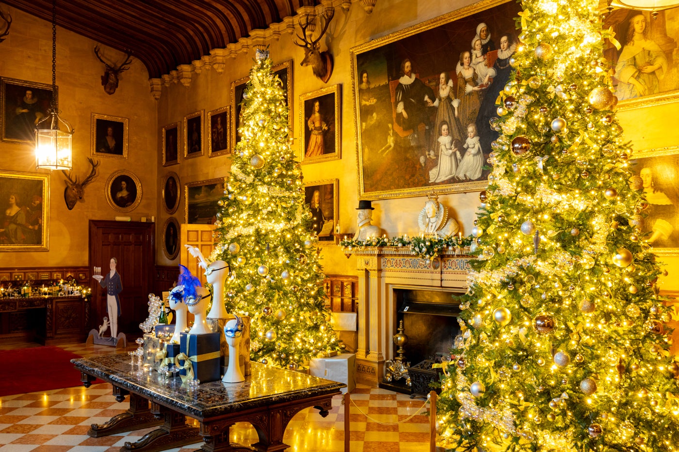 Two illuminated 16-ft Christmas trees flank a pietra dura table decorated with Venetian trees in Charlecote's Great Hall
