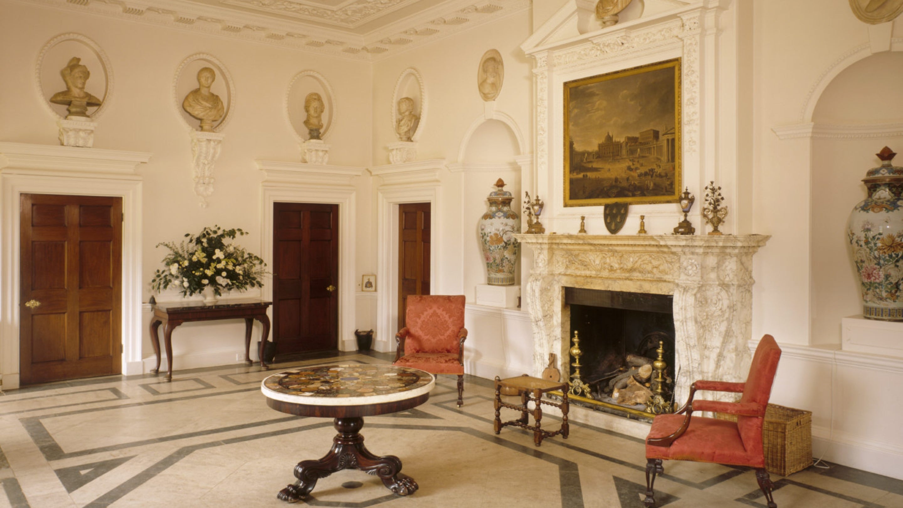 The Entrance Hall at Farnborough Hall with Roman busts set into the walls, a large fireplace and furnishings around the hall