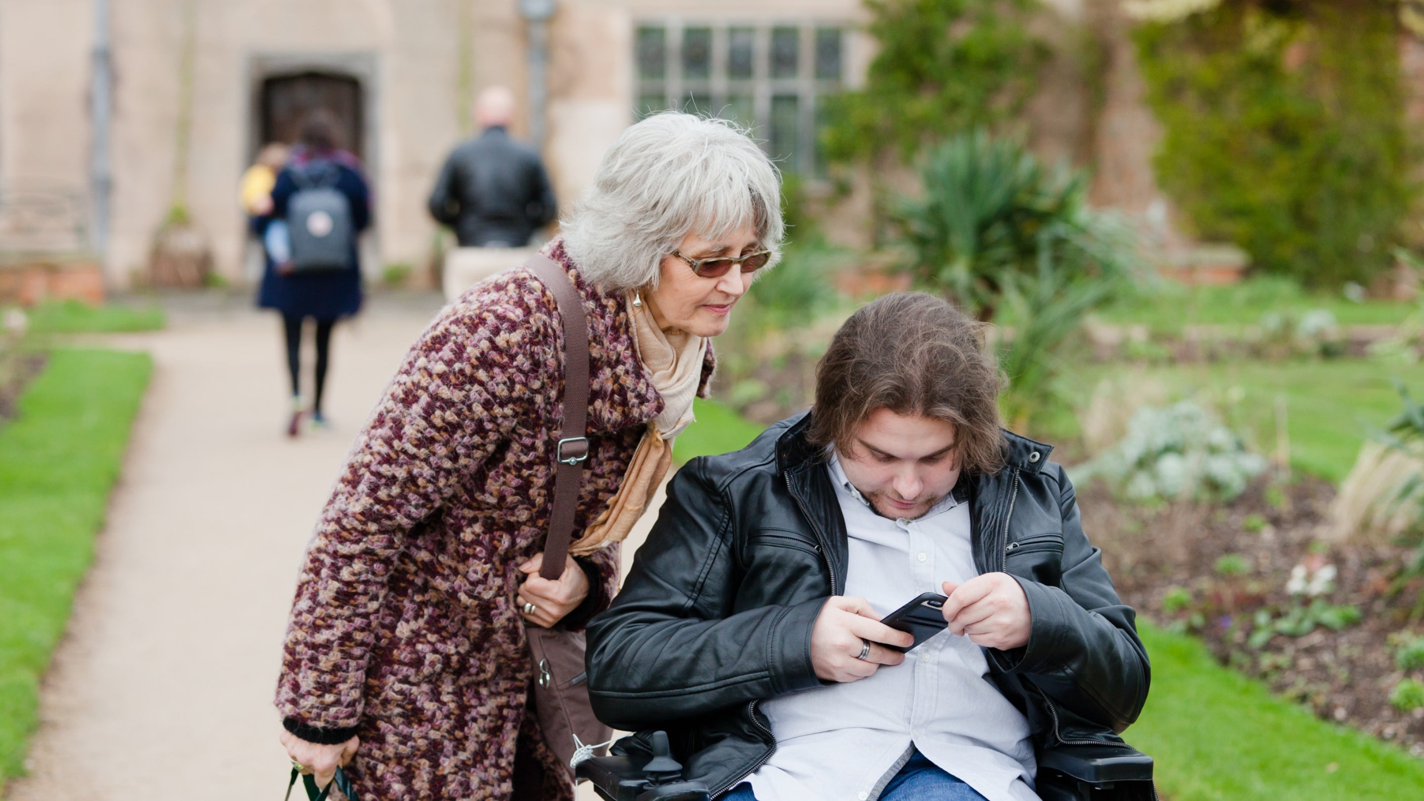 A lady and man in a wheelchair use a mobile phone in the garden at Packwood House in Warwickshire