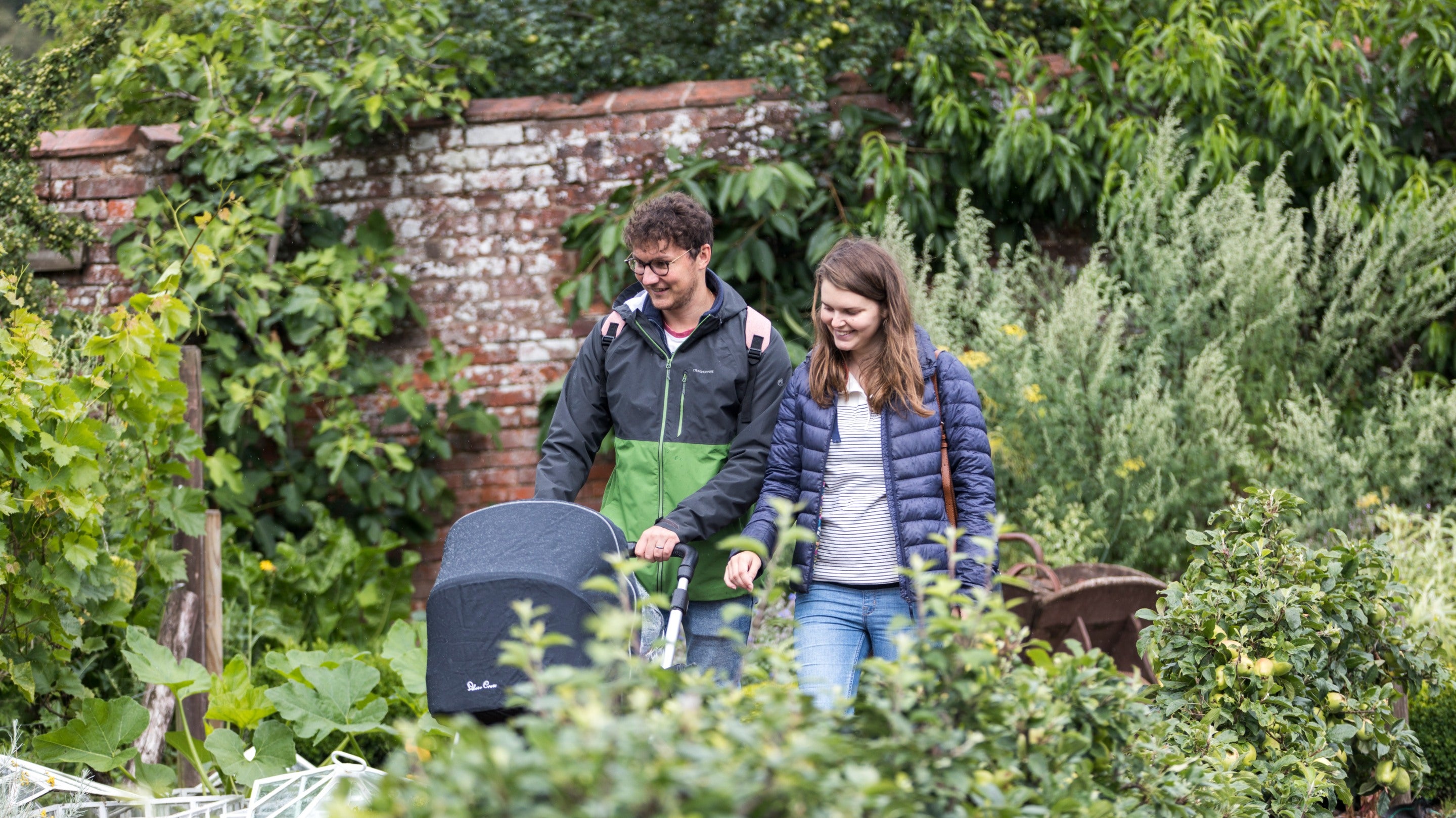 A couple pushing a pram in the Kitchen Garden at Packwood House, Warwickshire