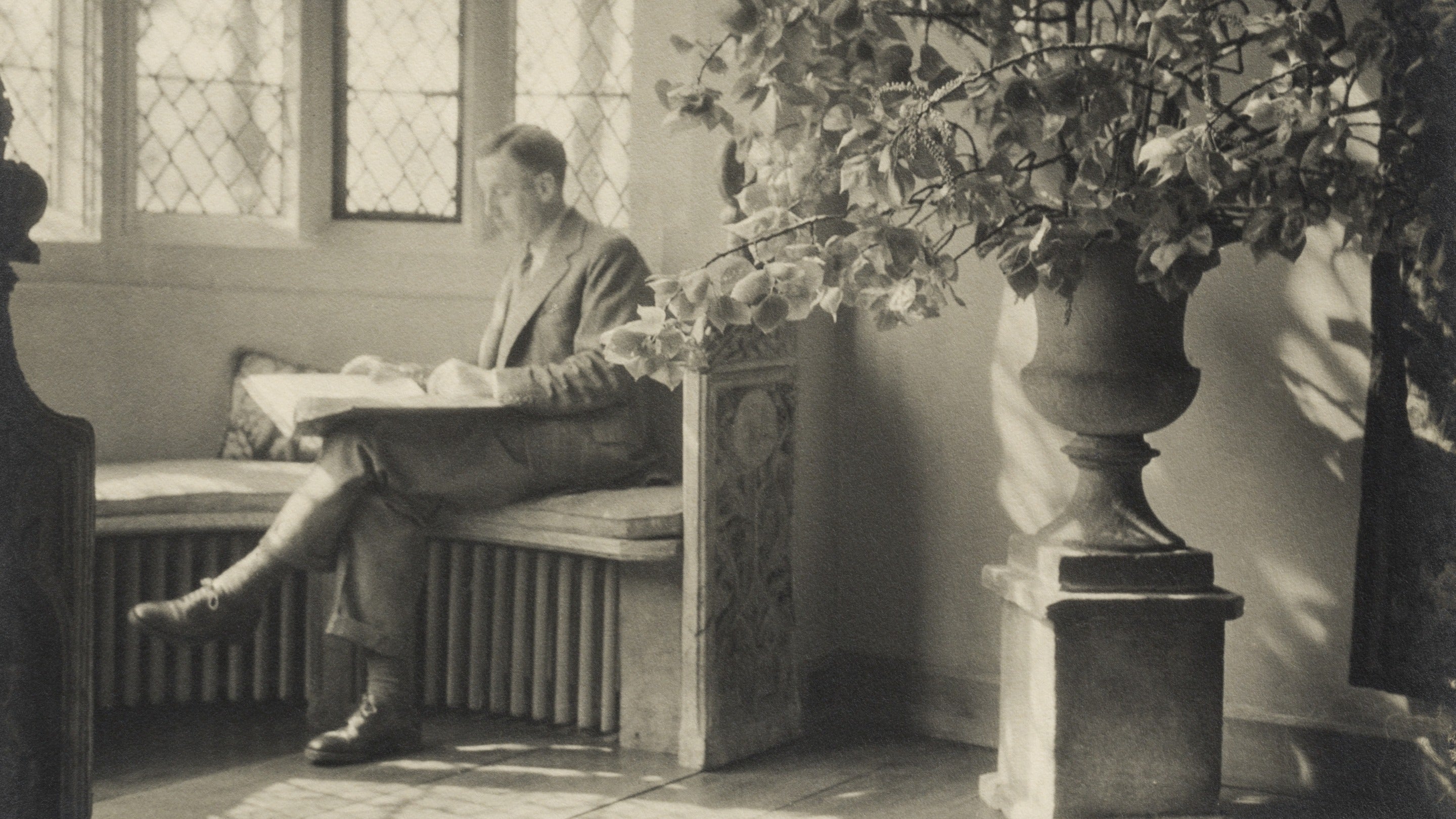 A black and white photograph of Graham Baron Ash sat reading a newspaper in the window of the Great Hall, Packwood House, Warwickshire.