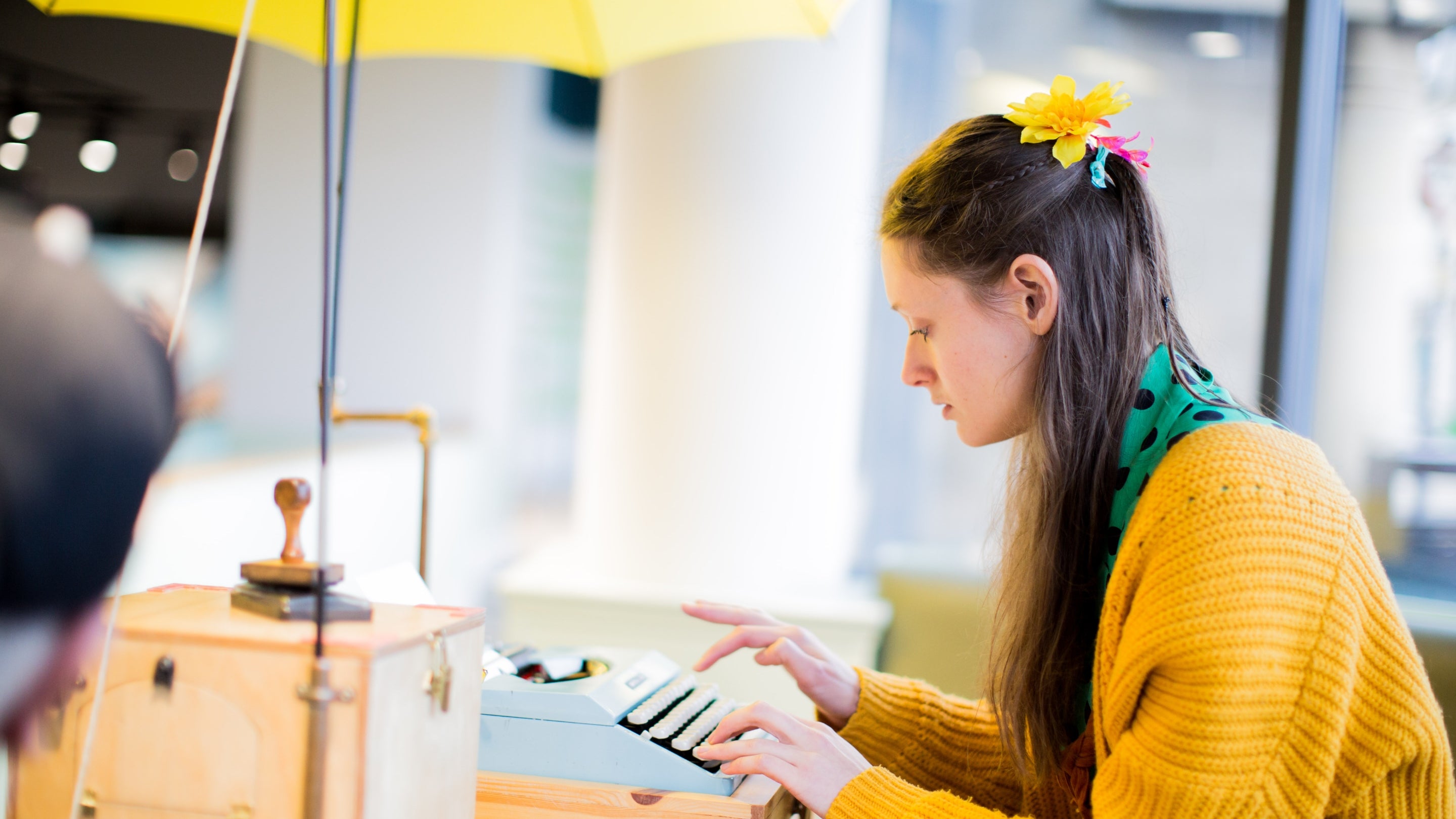A woman typing on an old typewriter under a yellow umberella
