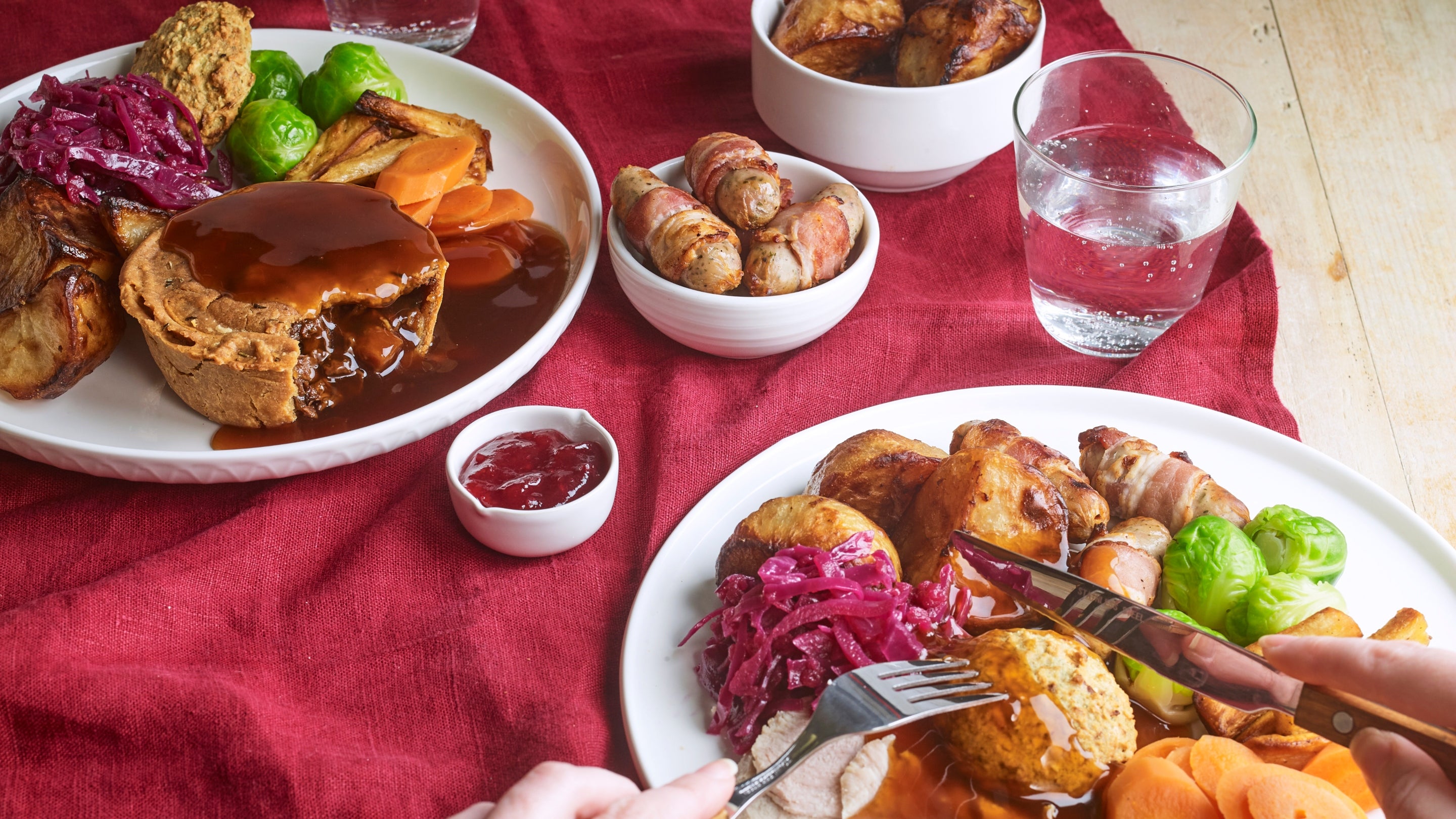 A person tucks into a Christmas lunch filled with turkey, roast potatoes and all the trimmings. On the table is a vegan pie dinner, and a side of pigs in blankets.