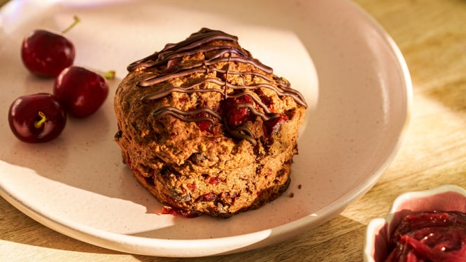 A National Trust chocolate and cherry scone on a plate with some cherries.