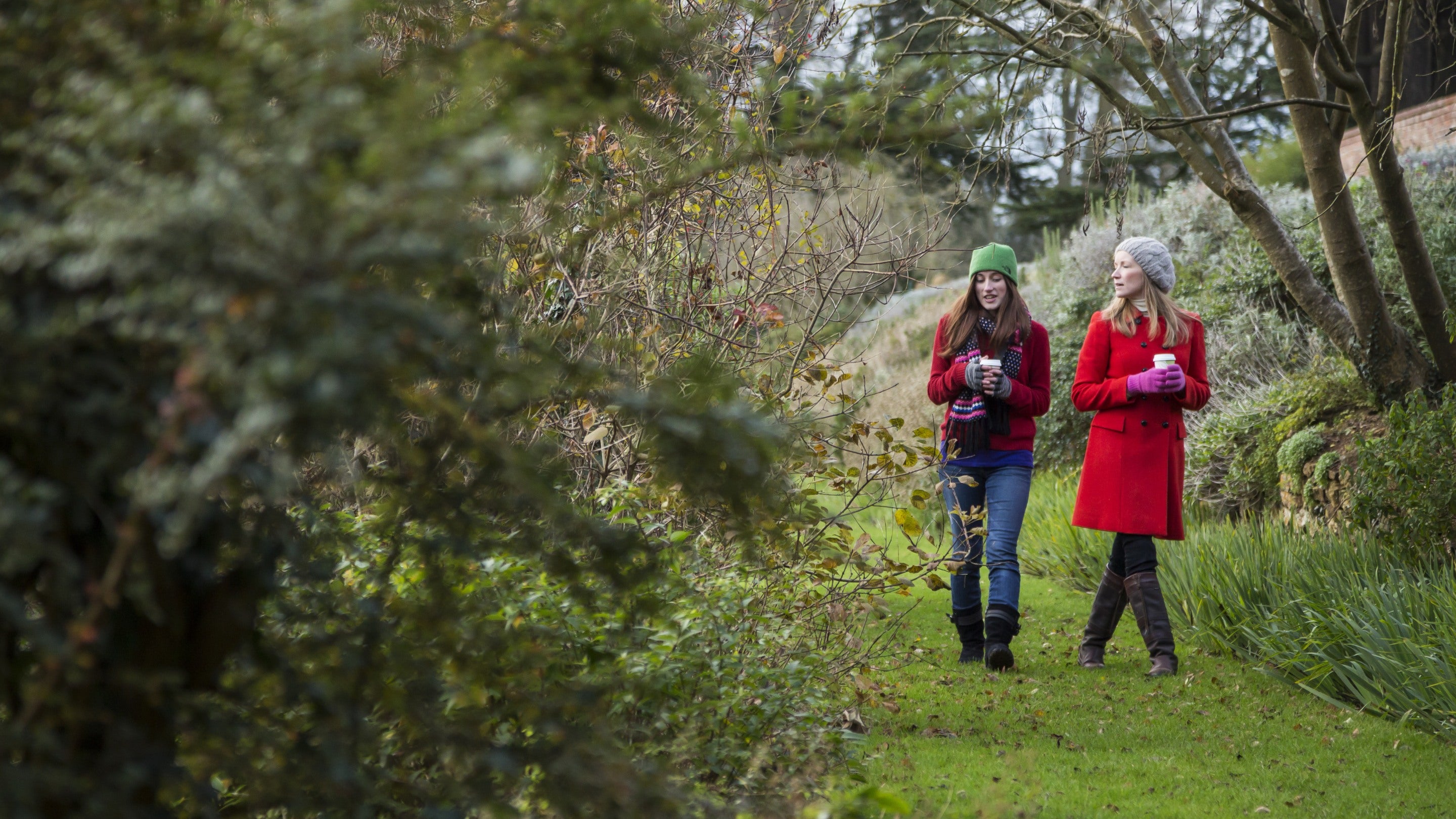 Two women carrying drinks, walking in the gardens at Upton House and Gardens, Warwickshire