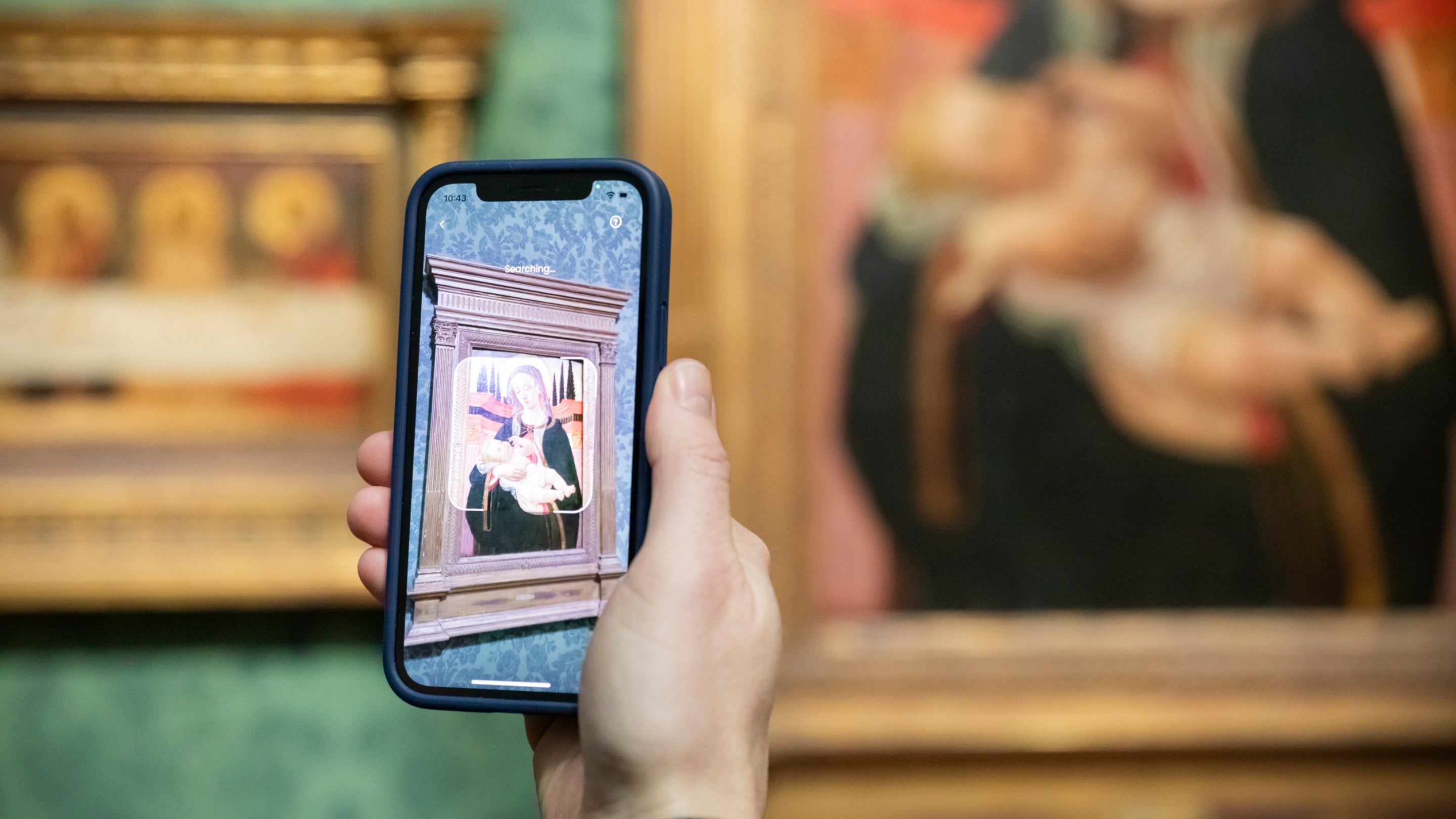 A hand holding a mobile phone scanning a painting at Upton House and Gardens using the Smartify app to bring up more information on the detail