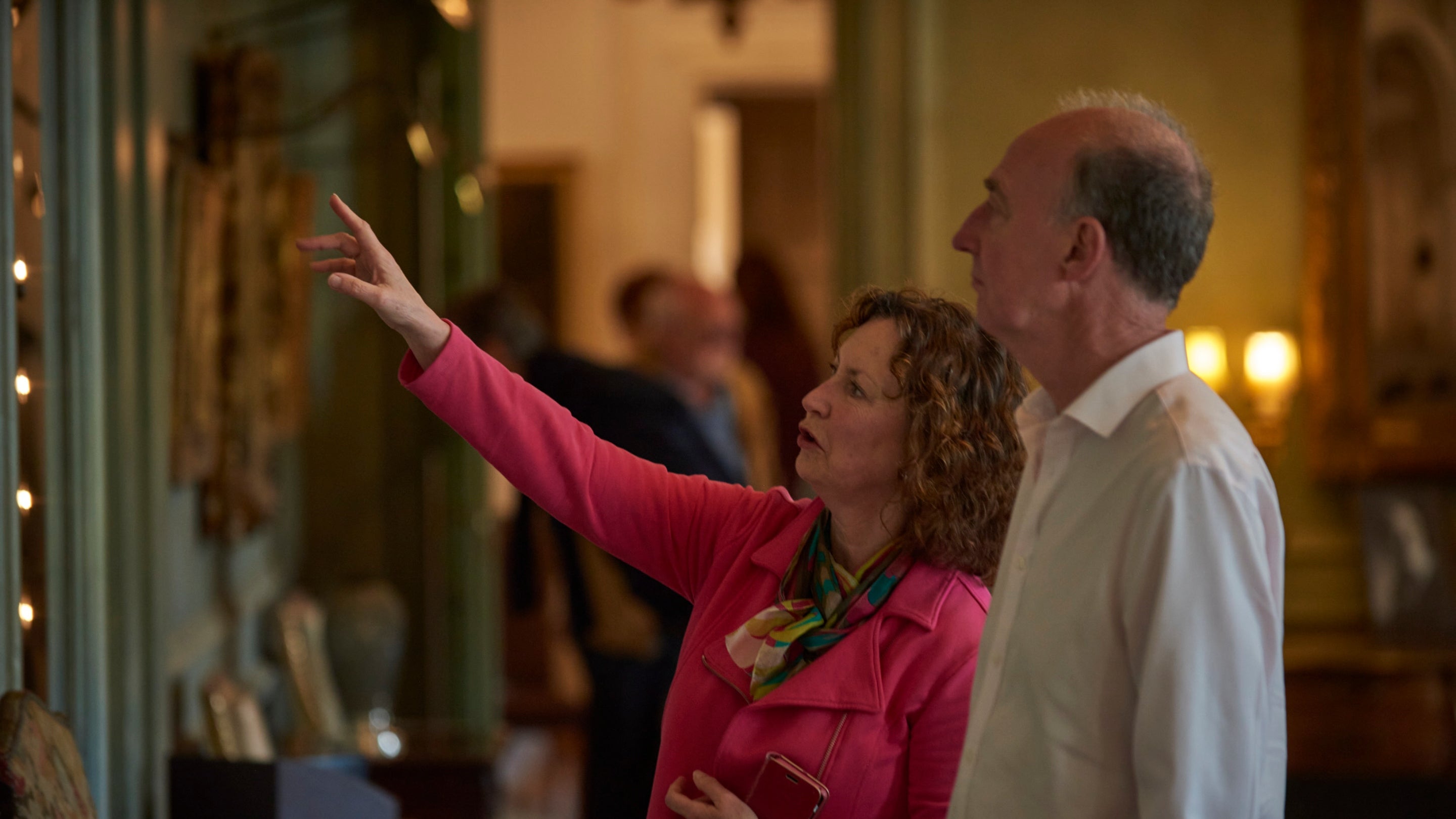 Two visitors stood side by side looking at a painting, one of them is pointing towards it.