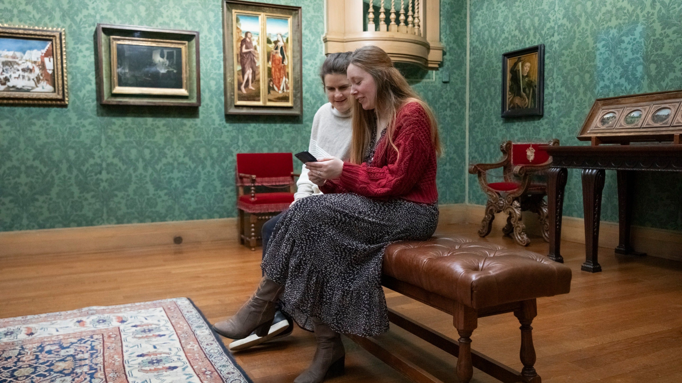 Two visitors sat in the Picture Gallery looking at the Smartify app. on a mobile phone in the Picture Gallery Upton House & Gardens, Warwickshire, 1814913