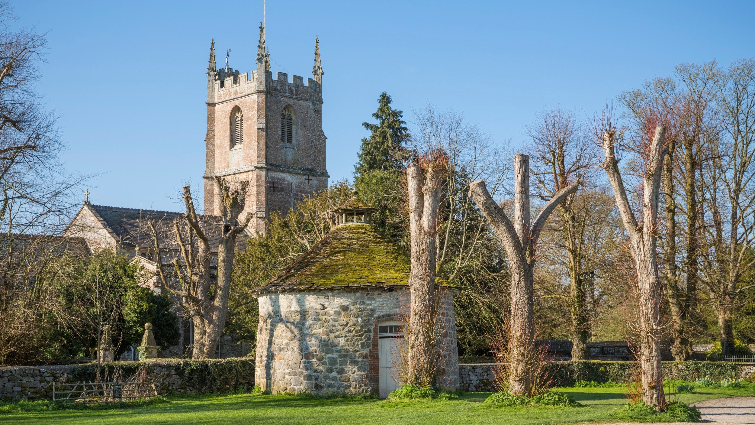 An old church, round dovecote and tree-lined avenue on a sunny spring day