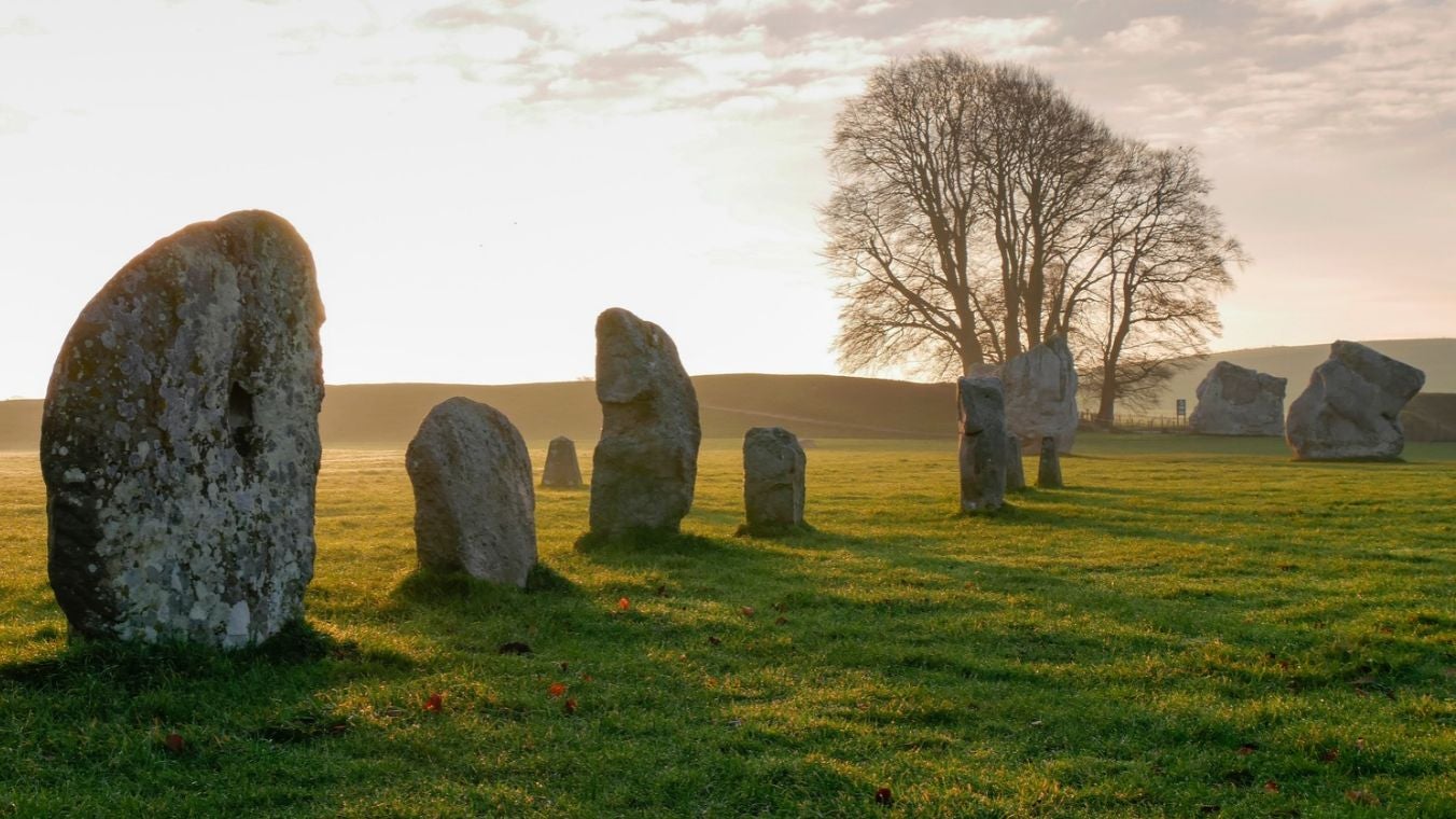 Standing stones in the SE sector at Avebury with bright early morning sunlight rising over the henge bank in the background