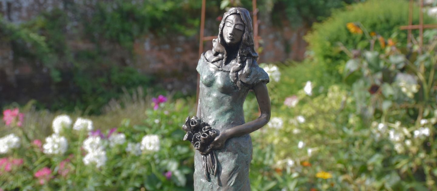 A sculpture of a woman holding a bunch of roses, set against a backdrop of colourful flowers and stone walls