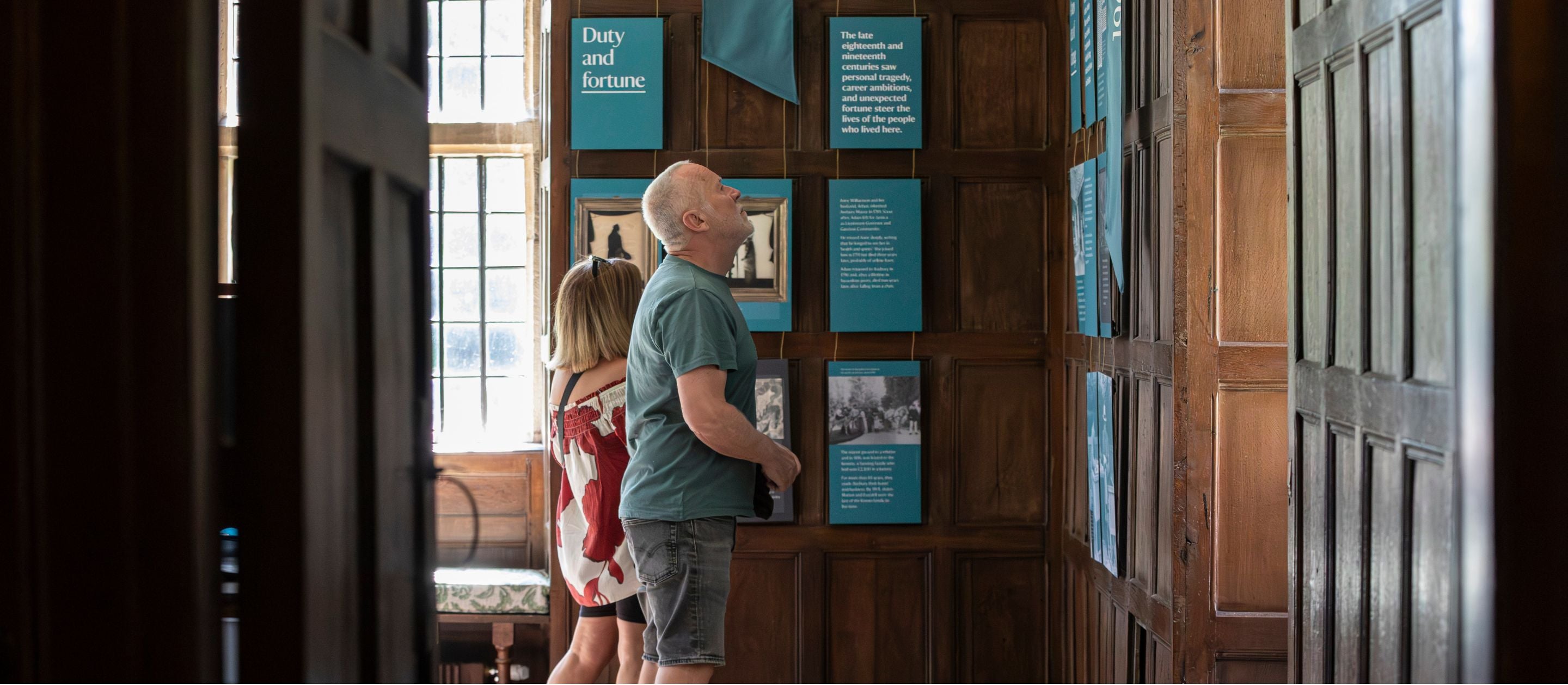 A man and a woman reading blue flags and interpretation panels hanging on the oak-panelled walls of the Great Parlour inside Avebury Manor