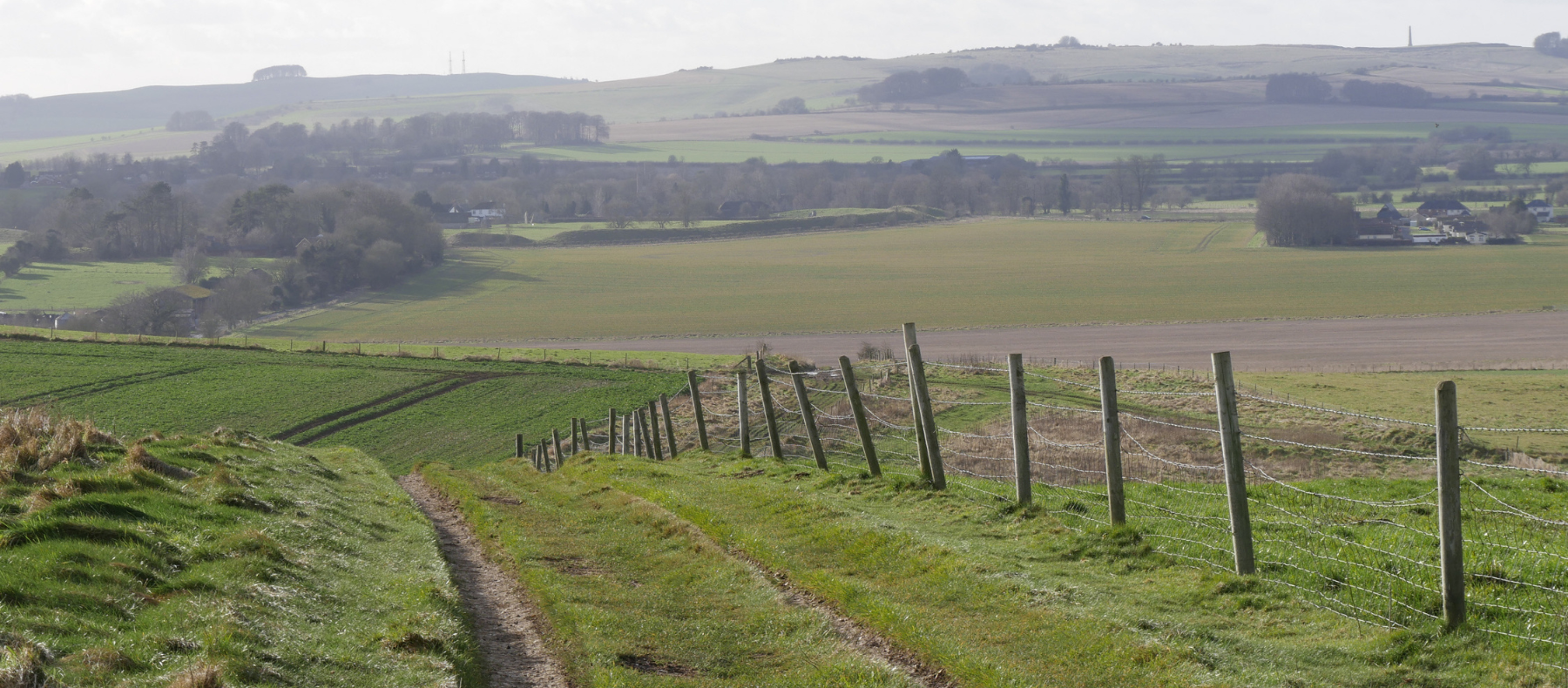 A wide landscape view from the Ridgeway looking back towards Avebury, with the henge and stones visible on the horizon.
