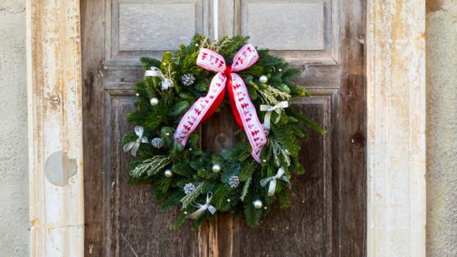 A Christmas wreath featuring green branches and red ribbons hanging on an old wooden door.