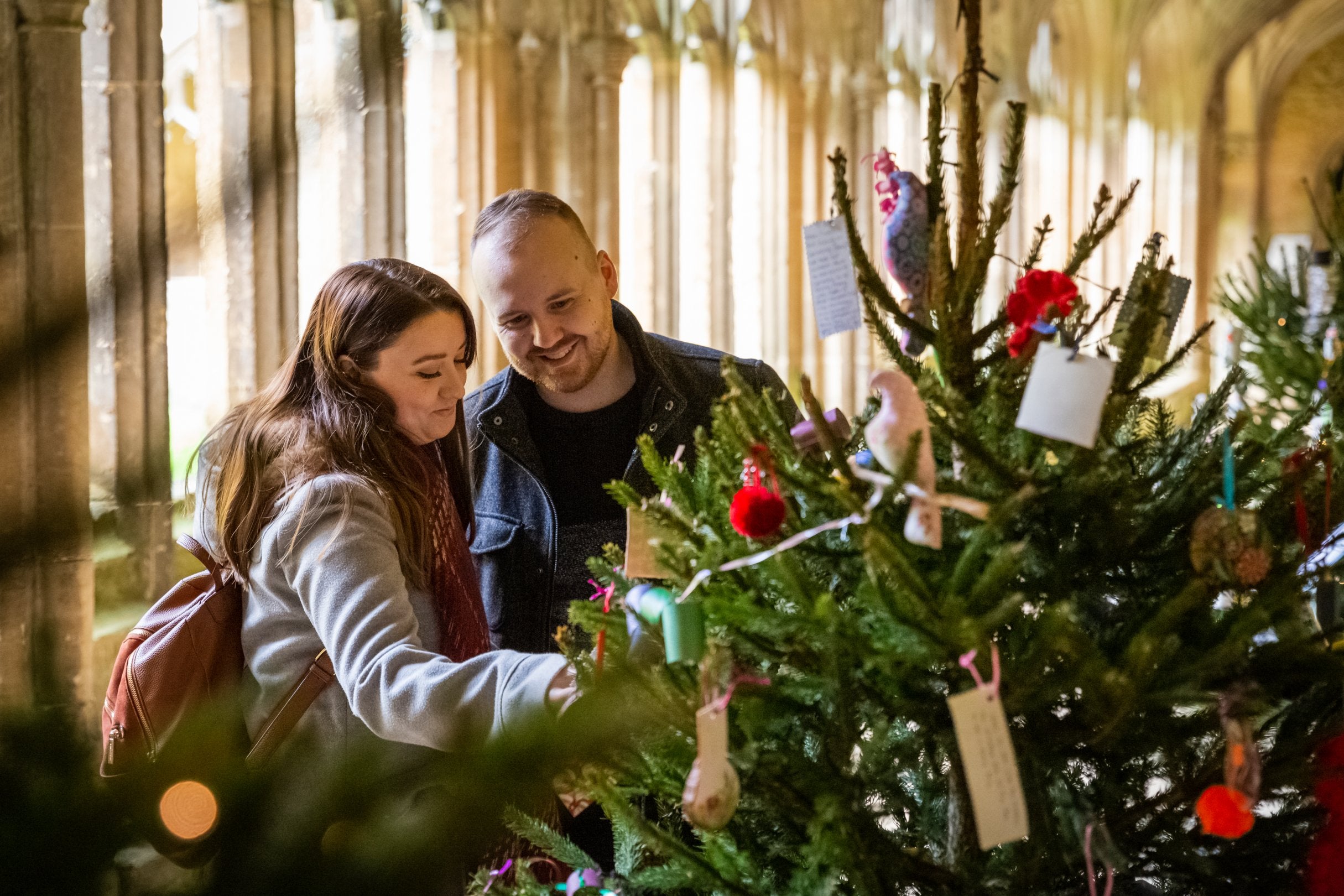 Two visitors in the cloister looking at one of the Christmas Trees decorated for Lacock's Community Christmas Tree Festival, Lacock Abbey, Wiltshire