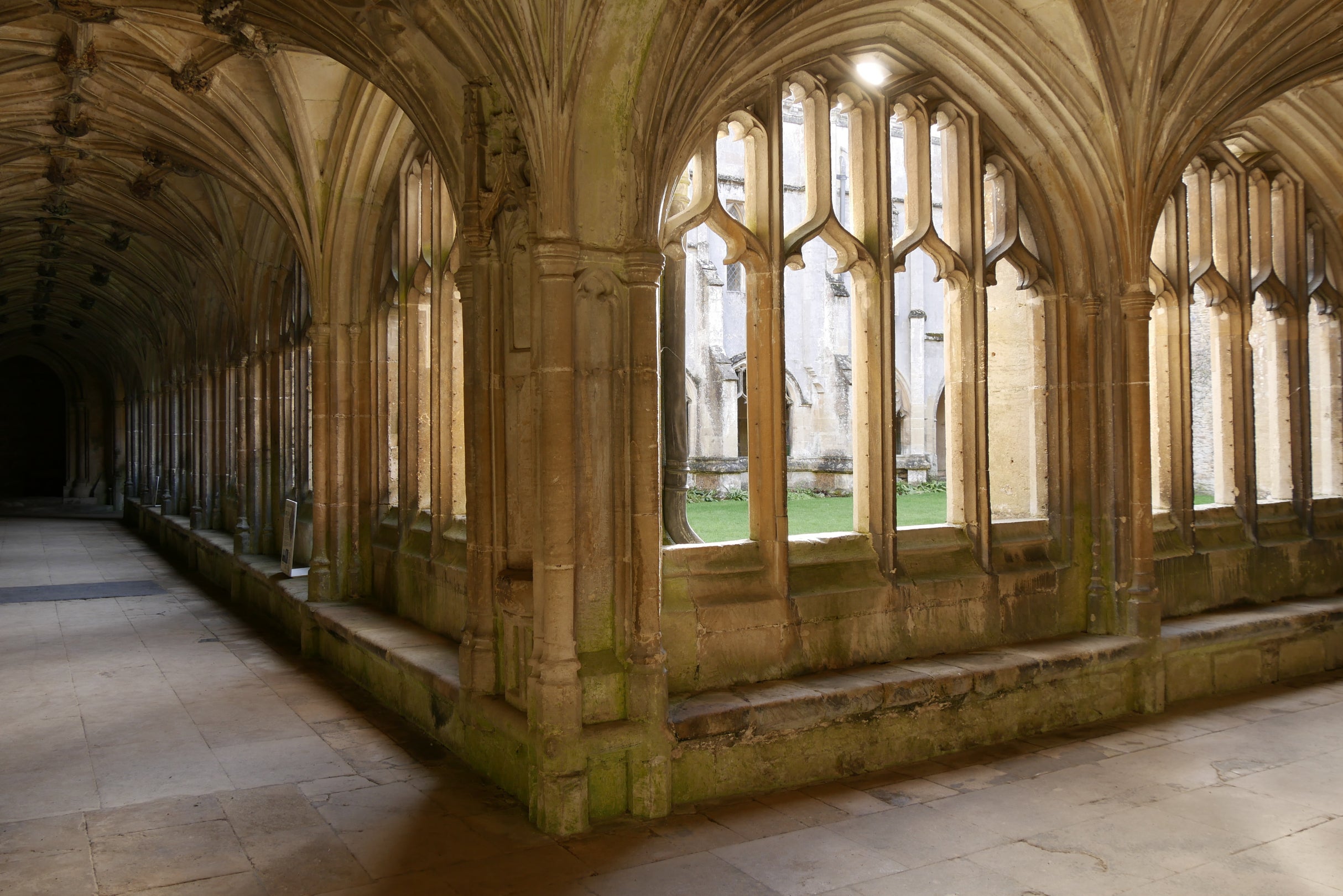 Looking down the Cloister walk at Lacock Abbey as light shines through the window, casting shadows on the floor.