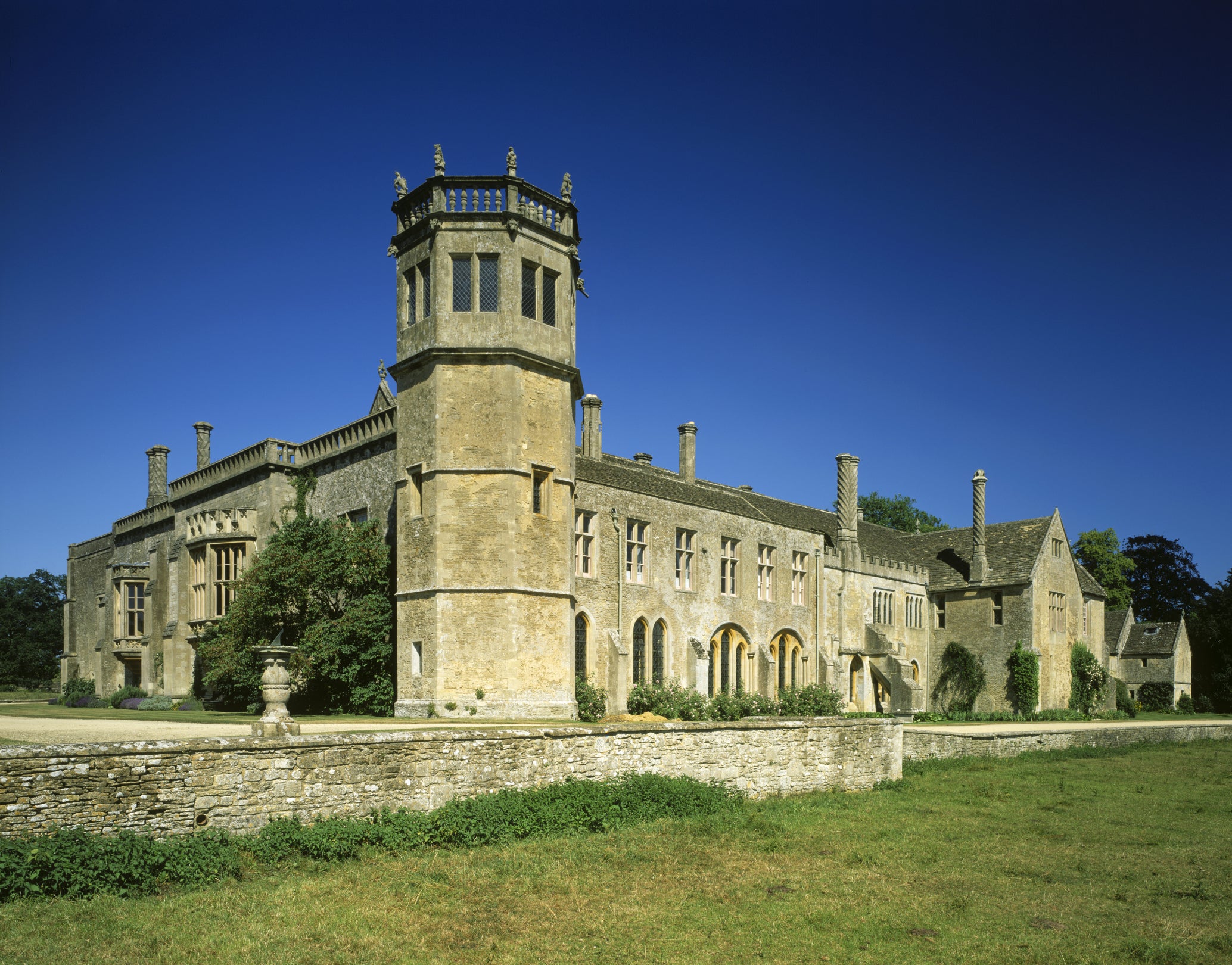 A view looking out from the abbey field towards the south corner of the abbey, with Sharington's Tudor tower at the centre. The sun is shining and the sky is blue.